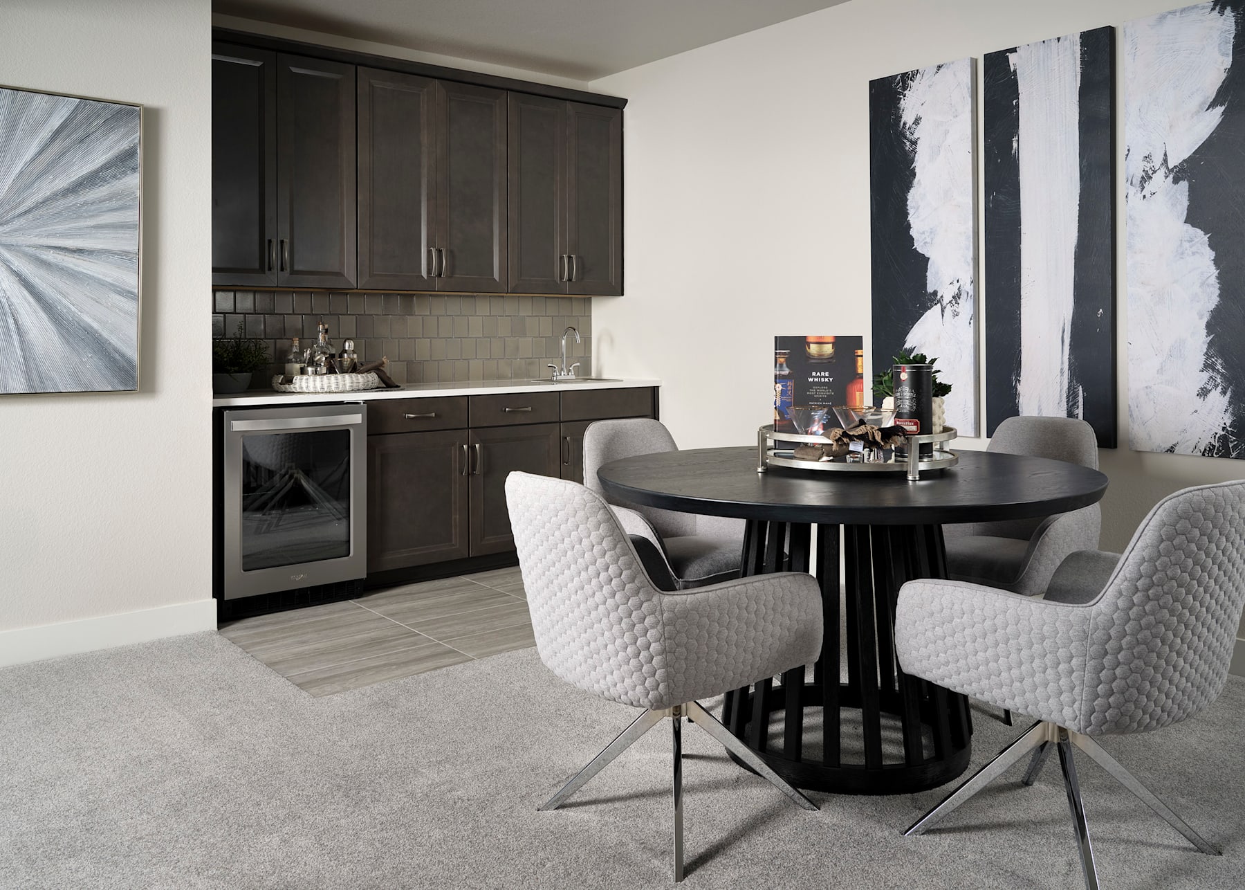 A modern kitchen with dark cabinets, a round dining table, and white upholstered chairs, set against a backdrop of abstract artwork.