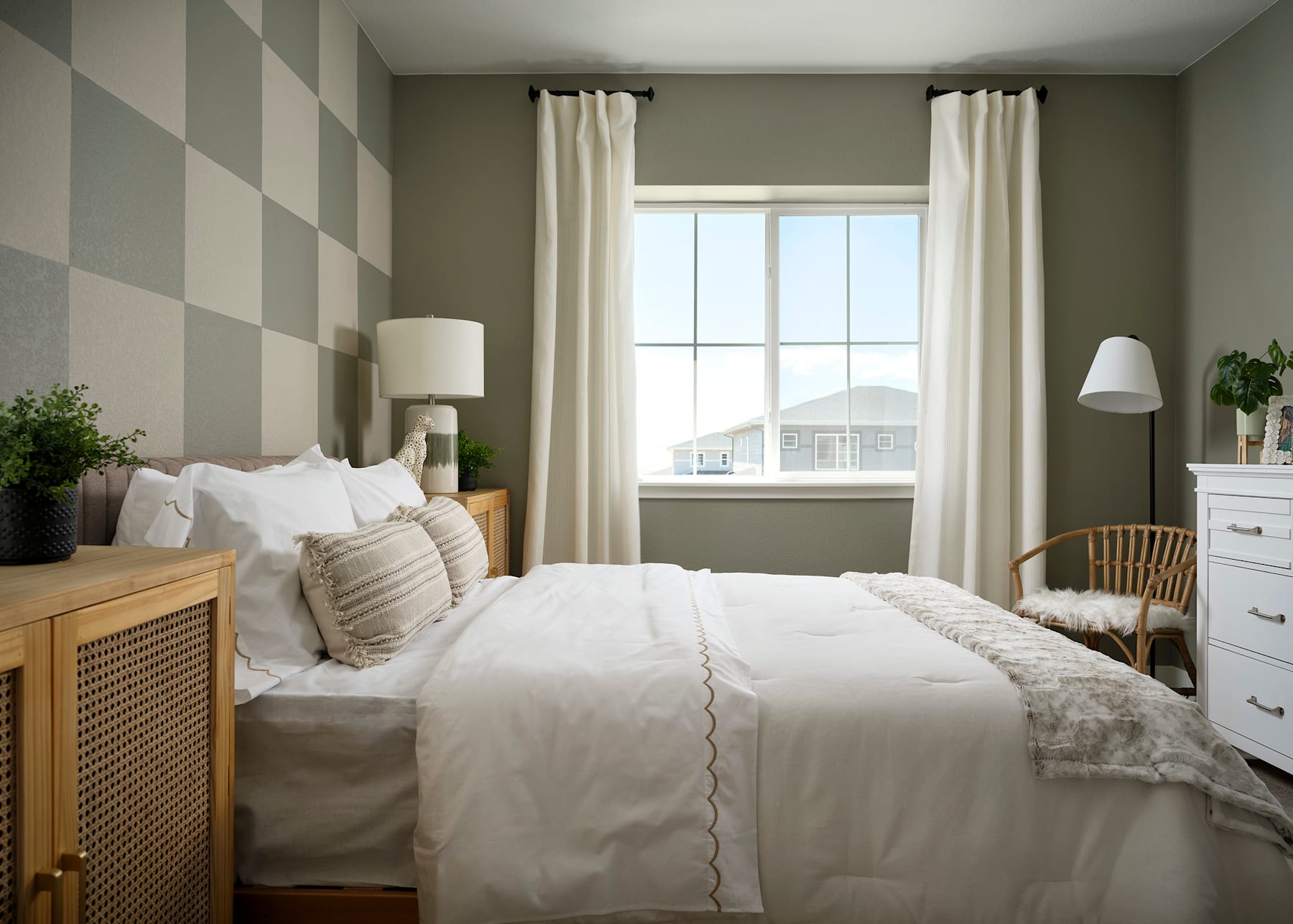 A cozy and inviting bedroom with a large window, a white bed with plush bedding, and a wooden dresser against the wall, creating a warm and serene atmosphere.