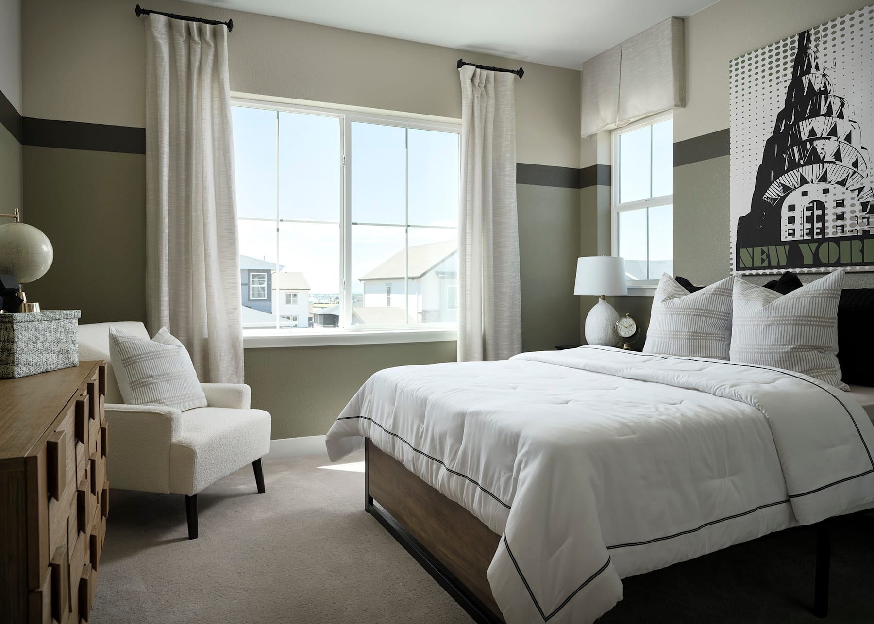 A cozy and modern bedroom with a large bed, white bedding, and a patterned accent wall featuring a castle-like design. The room also includes a comfortable armchair and large windows providing natural light.