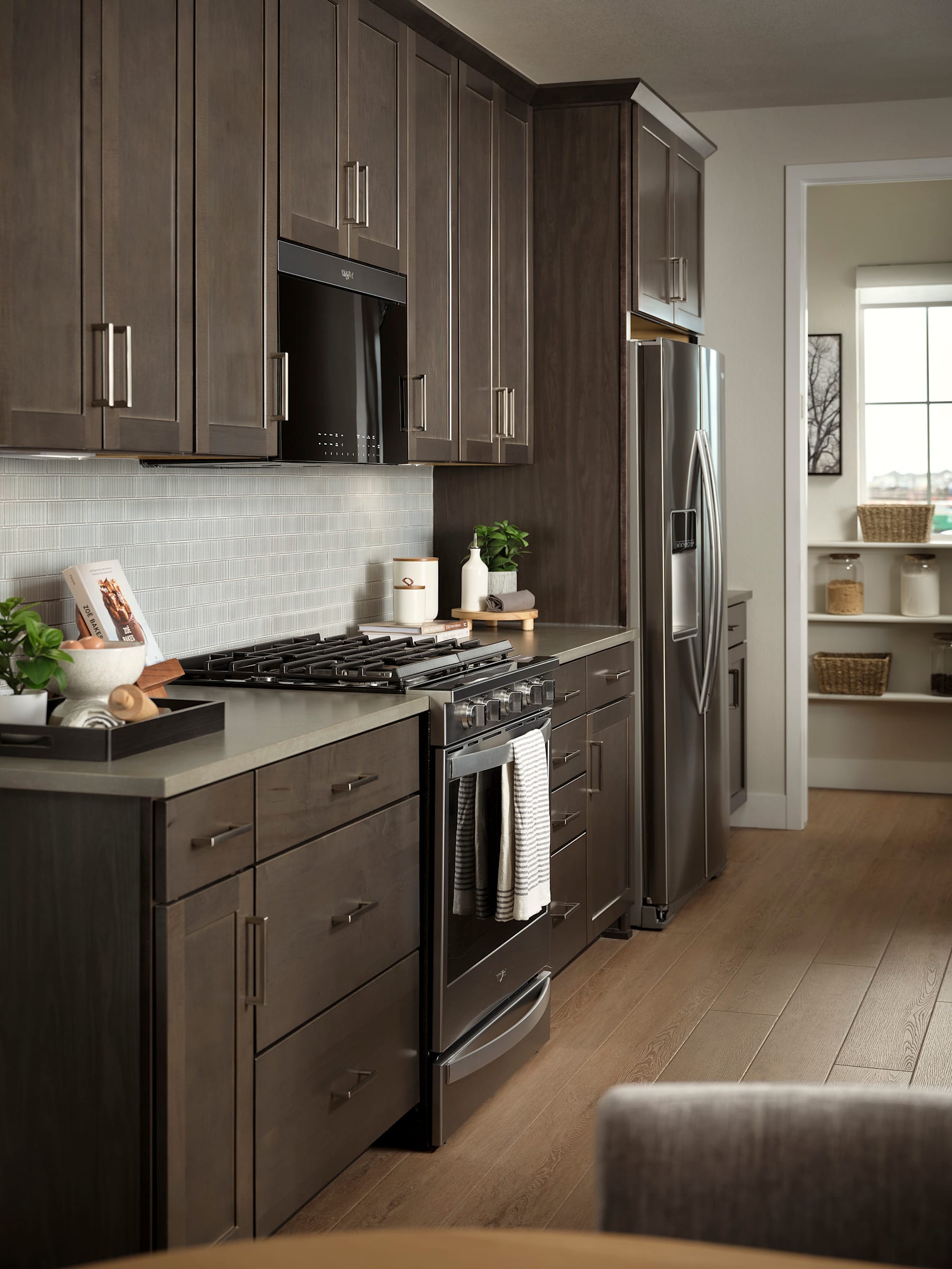 A modern and well-equipped kitchen with dark wood cabinets, stainless steel appliances, and a tiled backsplash, set against a light-colored hardwood floor and walls.