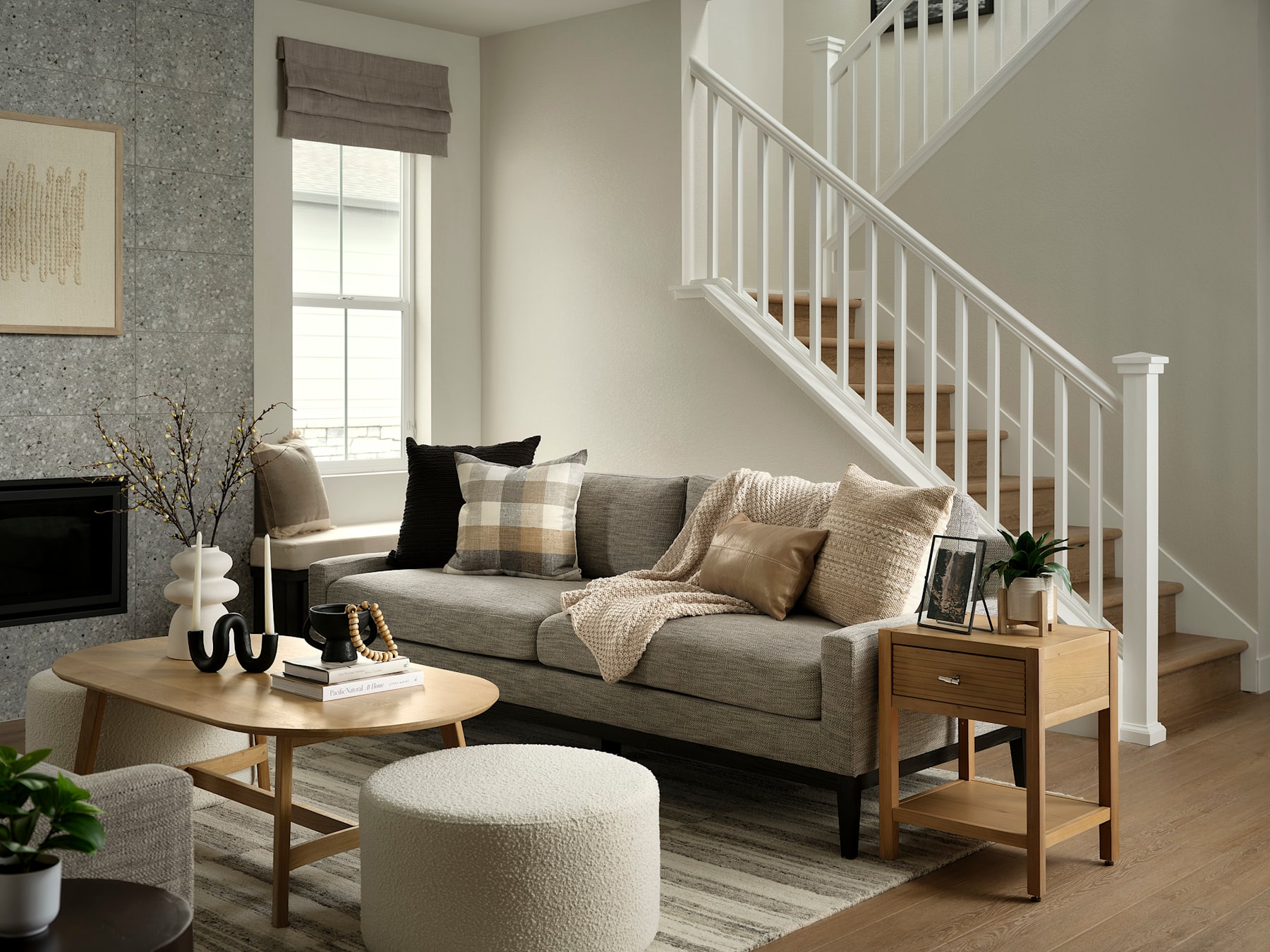 A cozy living room with a gray sofa, wooden side tables, and a staircase in the background, creating a warm and inviting atmosphere.