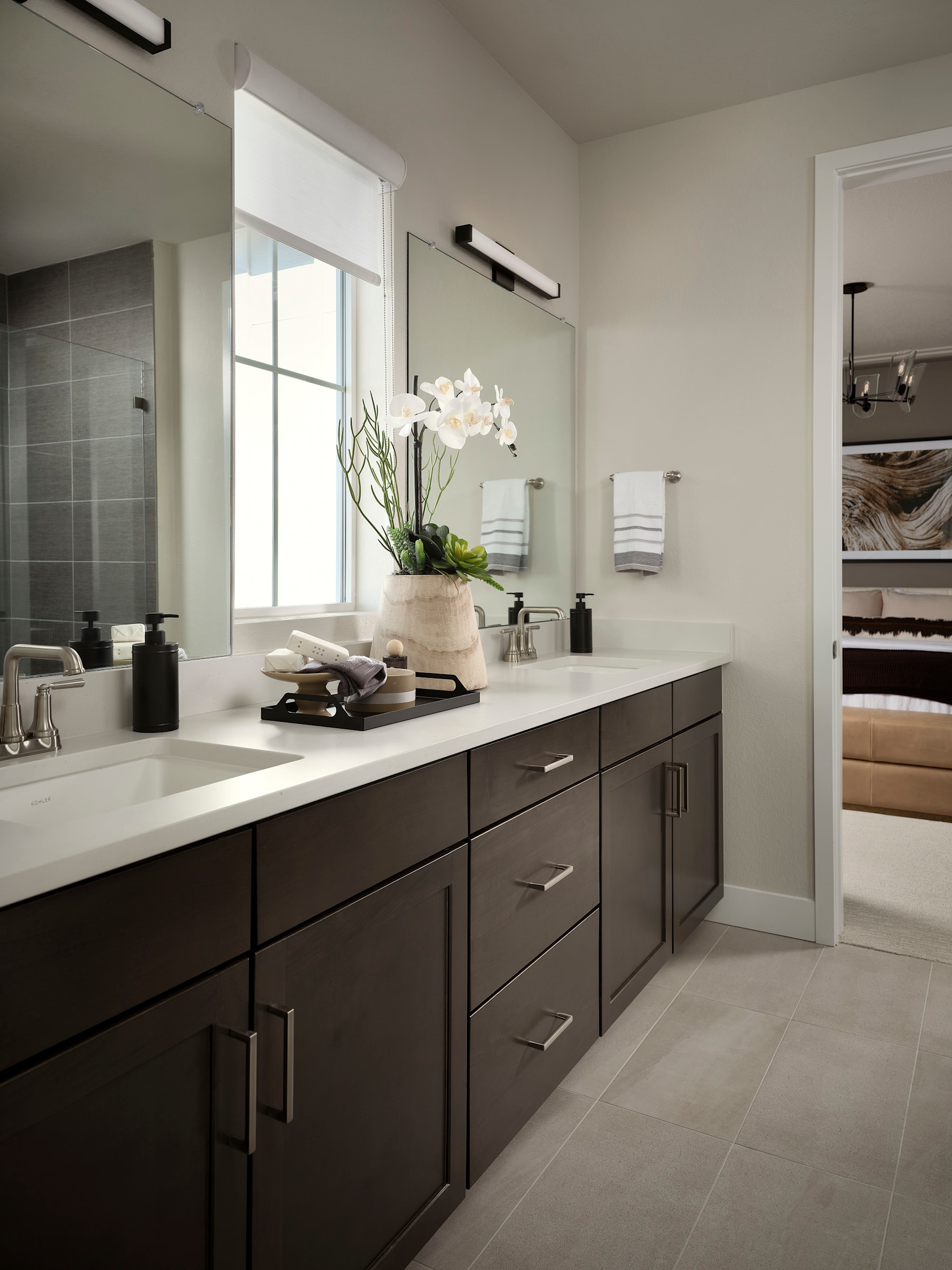 A modern and sleek bathroom with dark wood cabinets, a white countertop, and a large window providing natural light. The room features a minimalist design with a potted plant and other decorative elements.