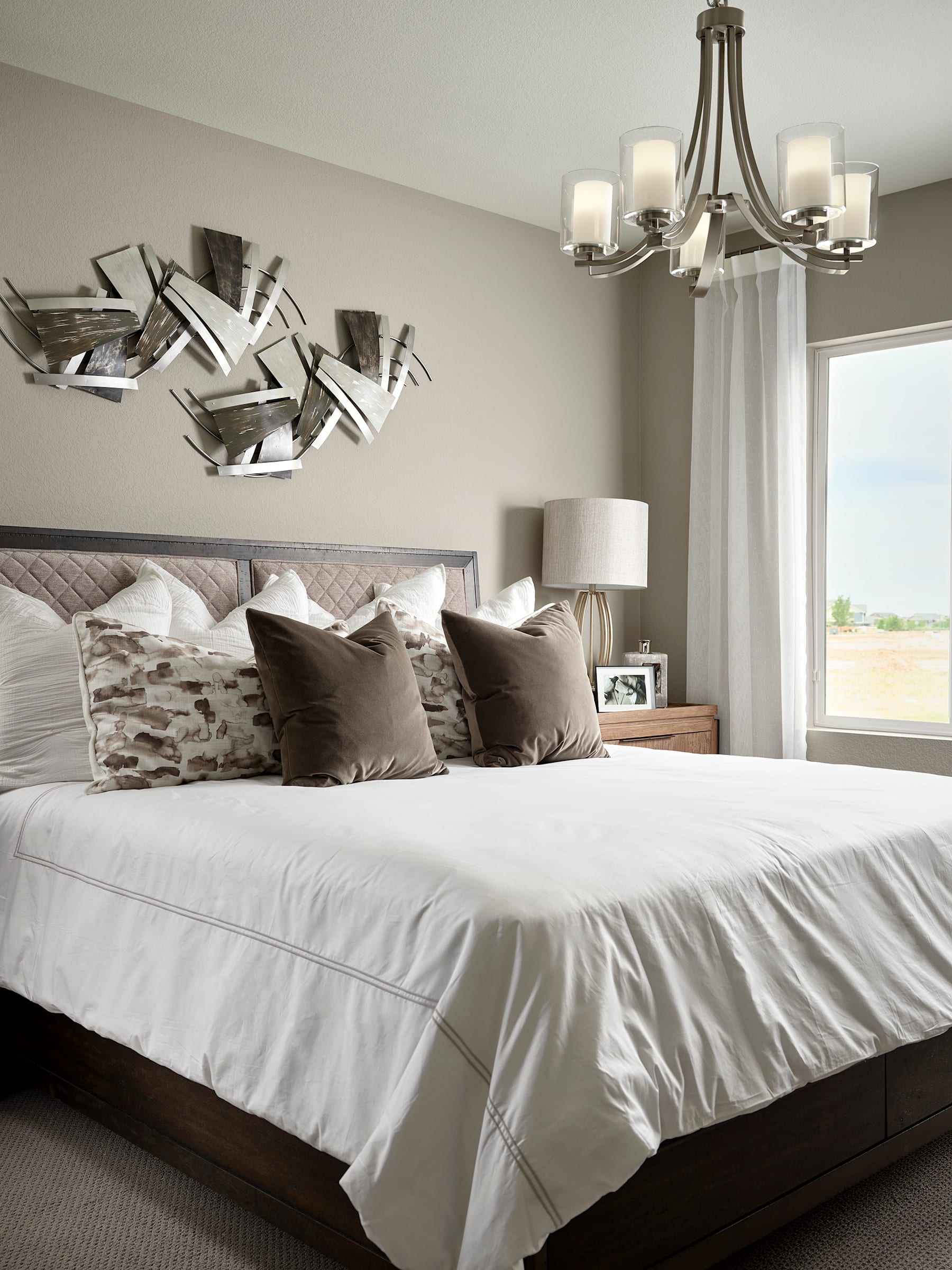 A spacious and elegantly designed bedroom with a large bed, plush bedding, and a striking modern light fixture overhead, complemented by a decorative wall art piece.
