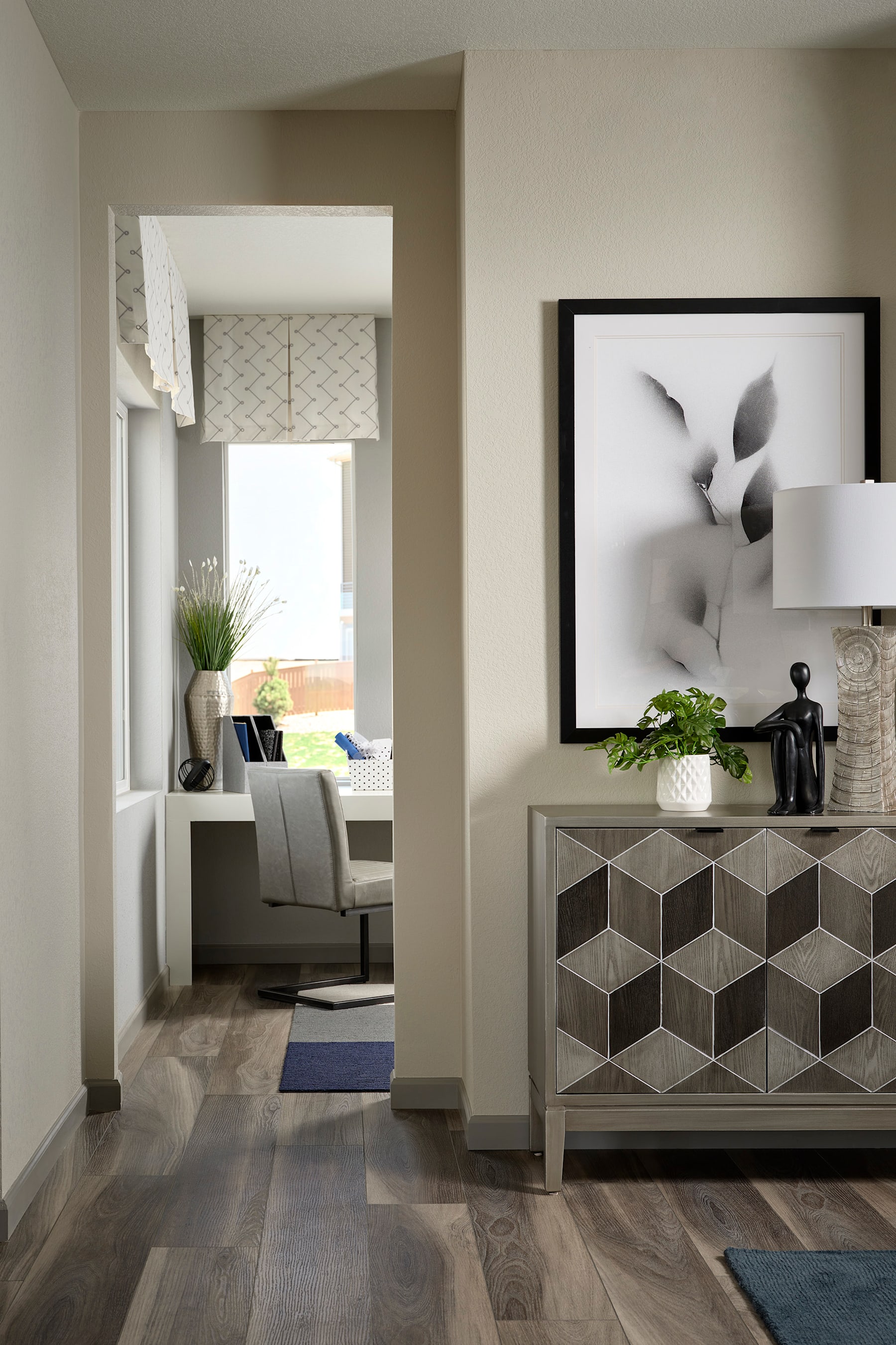 A modern and minimalist living room with a geometric patterned cabinet, a framed abstract artwork, and a cozy seating area visible in the background.