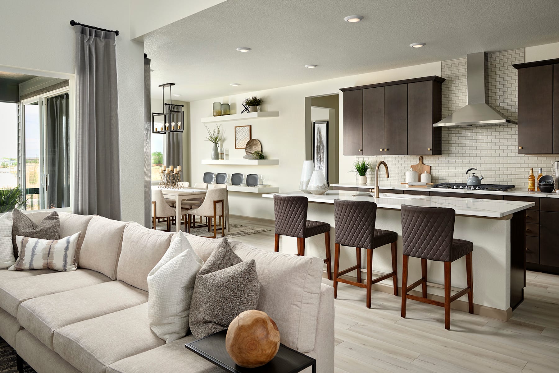 A cozy and modern open-concept living room and kitchen area with a large white sectional sofa, dark wood cabinetry, and a breakfast bar with stools.