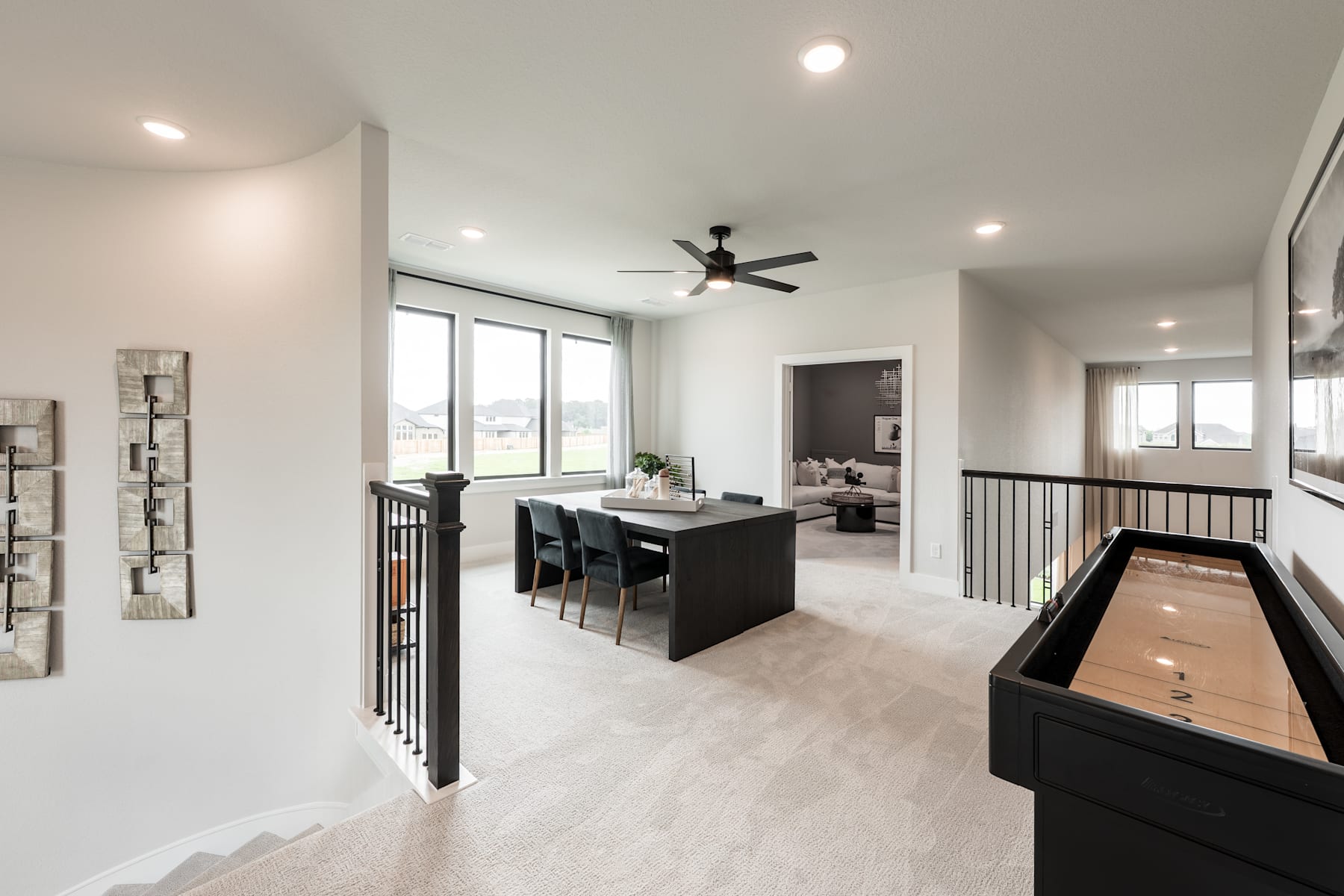 A modern, open-concept living space with a dining area, a ceiling fan, and a foosball table in the foreground, surrounded by neutral-toned walls and floors.