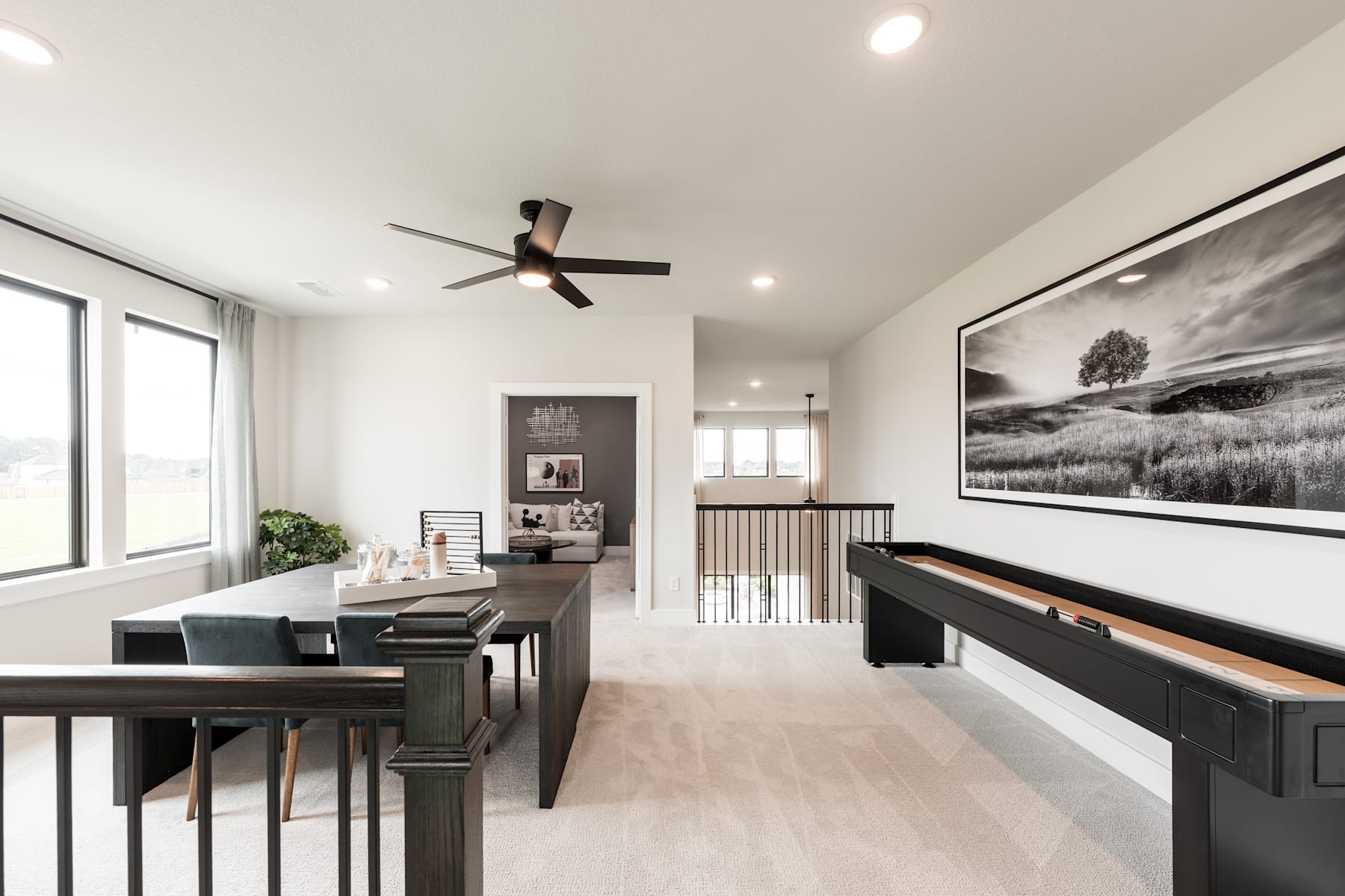 A modern and minimalist living room with a large black-and-white landscape artwork, a ceiling fan, and a wooden dining table with chairs.