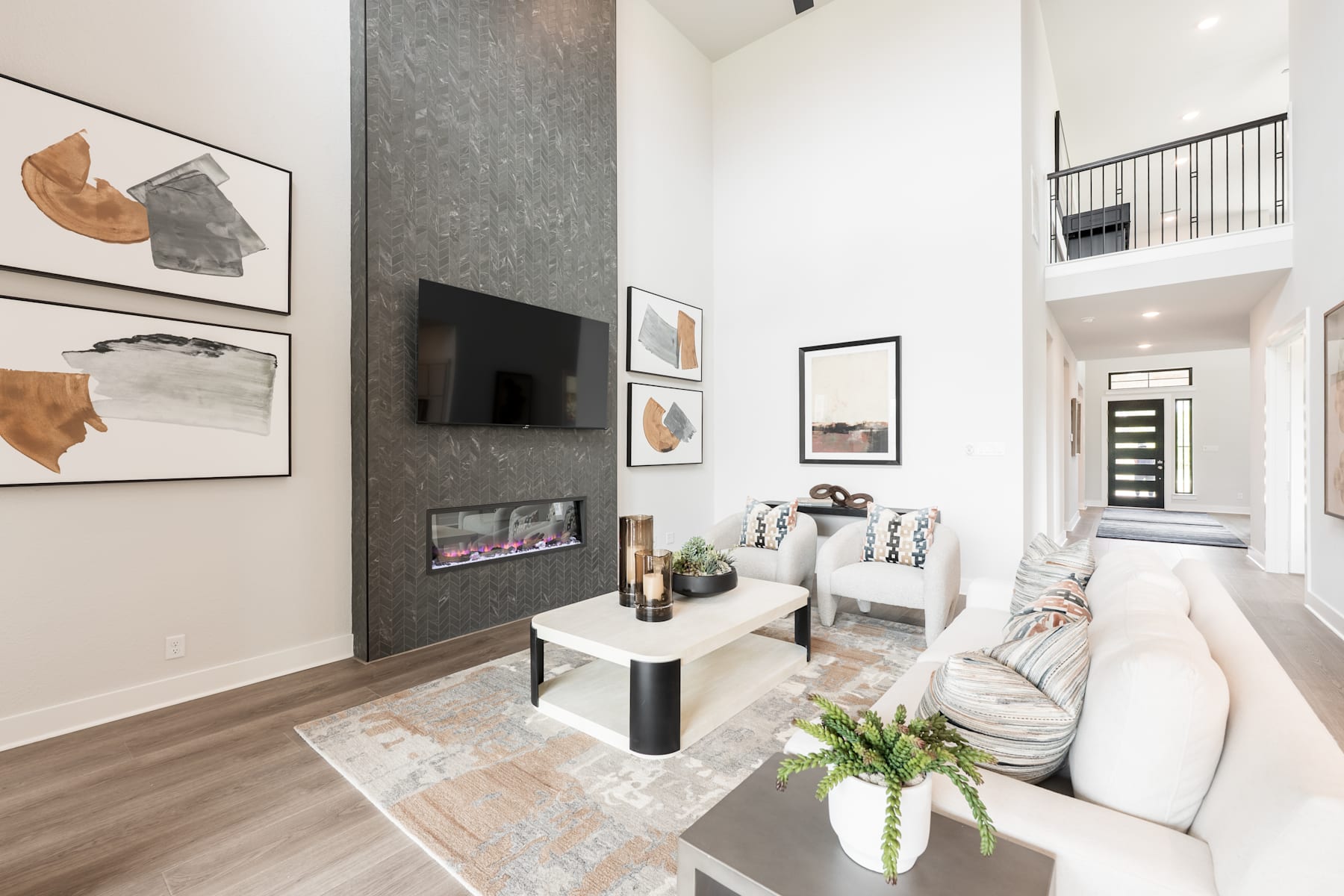 A modern and minimalist living room with a white sofa, abstract artwork on the walls, and a sleek coffee table in the foreground, set against a backdrop of a tall gray accent wall and a staircase leading to an upper level.