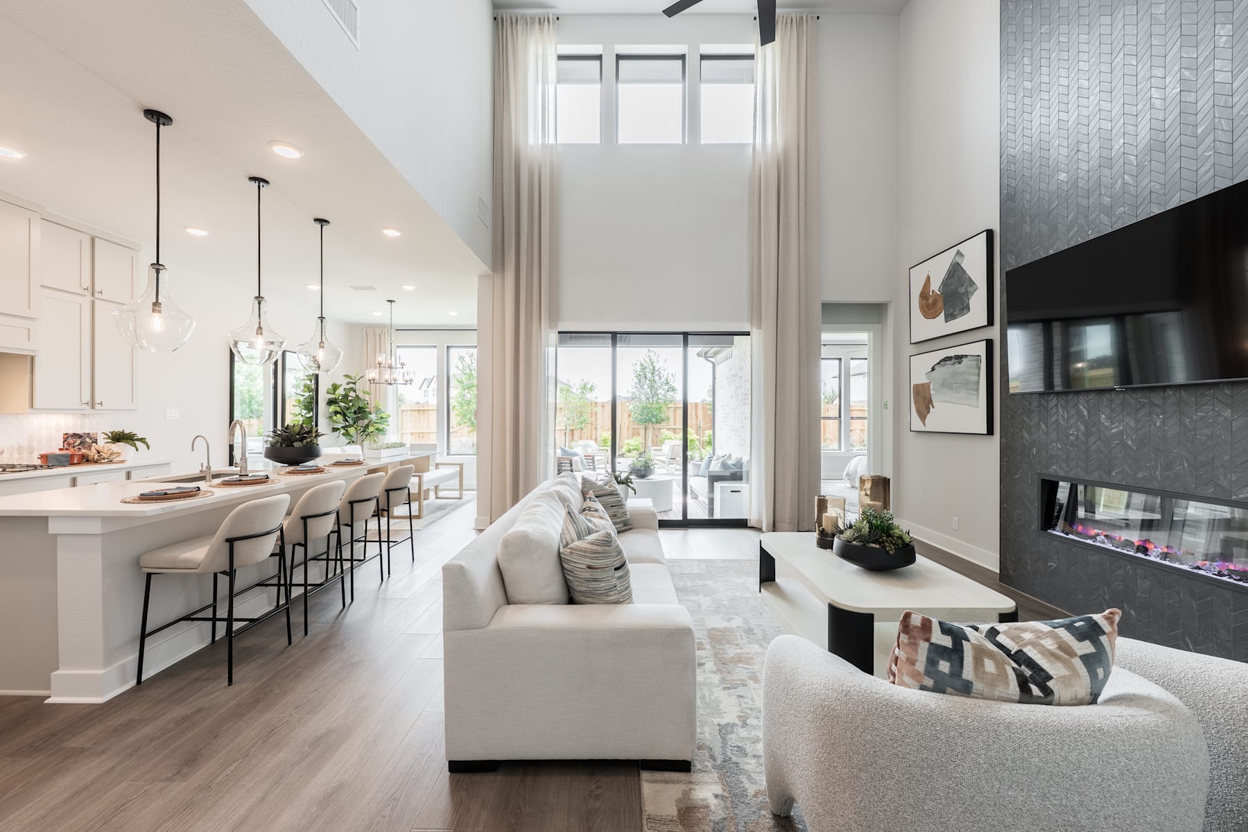 A modern, open-concept living space with a kitchen, dining area, and living room, featuring a neutral color palette, sleek furnishings, and large windows that allow natural light to flood the room.