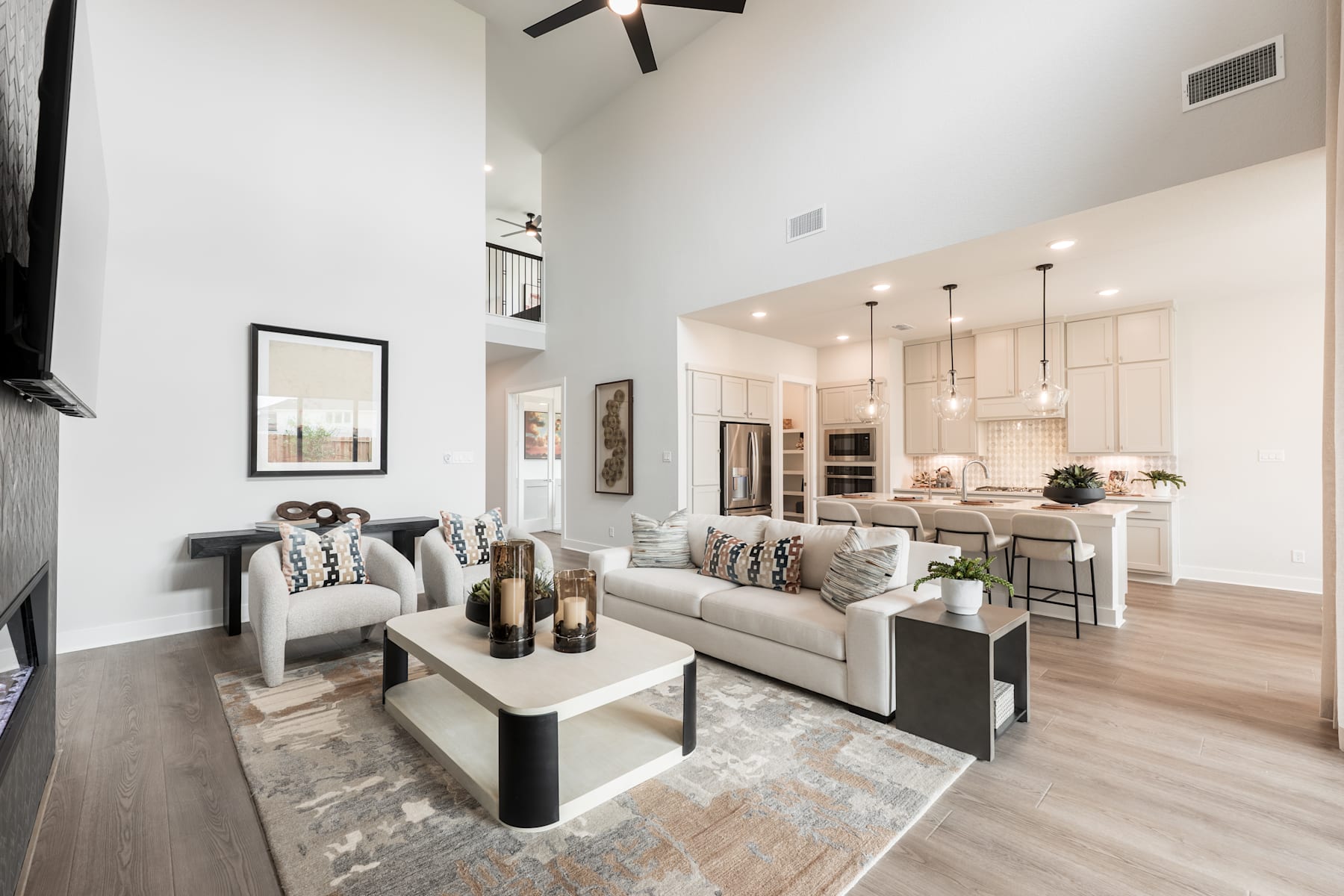A modern and stylish living room with a cozy sofa, a coffee table, and a kitchen visible in the background, featuring light-colored walls, hardwood floors, and pendant lighting.