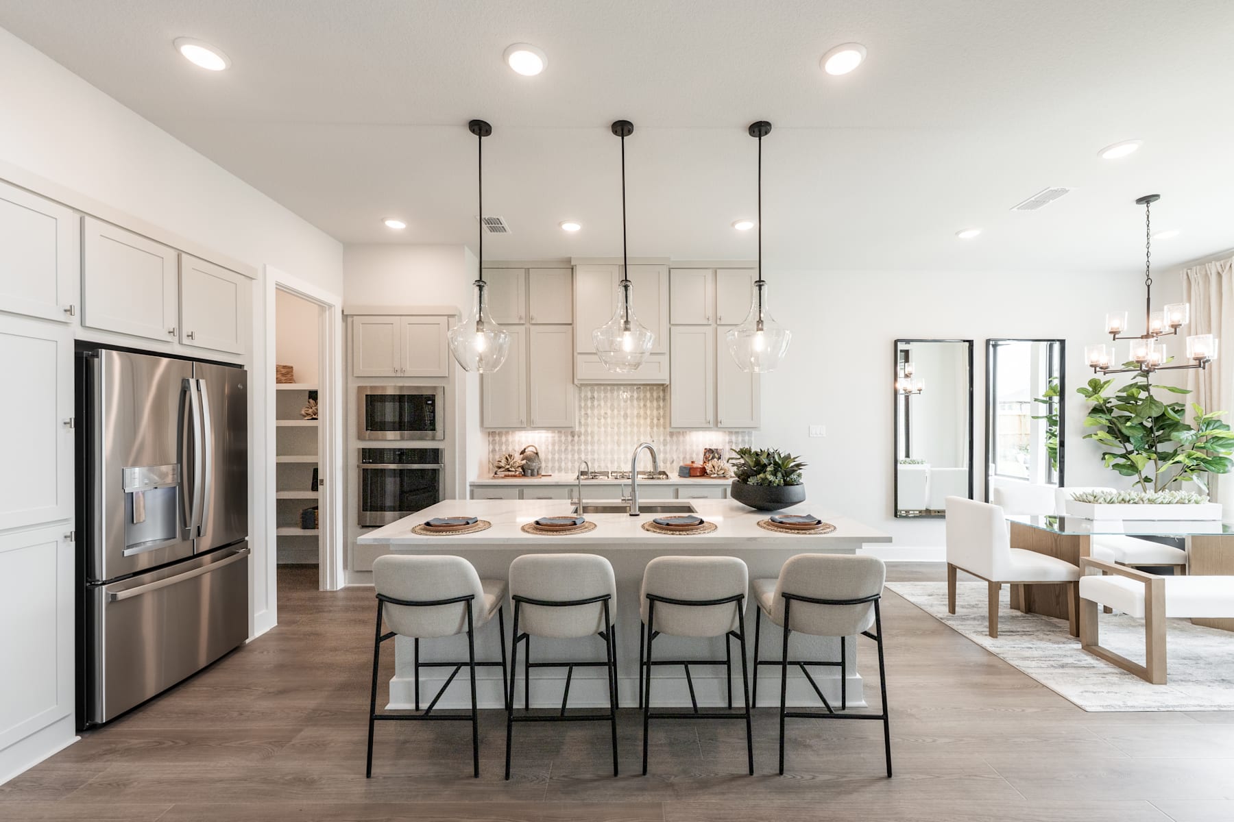 A modern, open-concept kitchen with stainless steel appliances, white cabinets, and a large island with bar stools, surrounded by a bright and airy space with pendant lighting and a dining area.