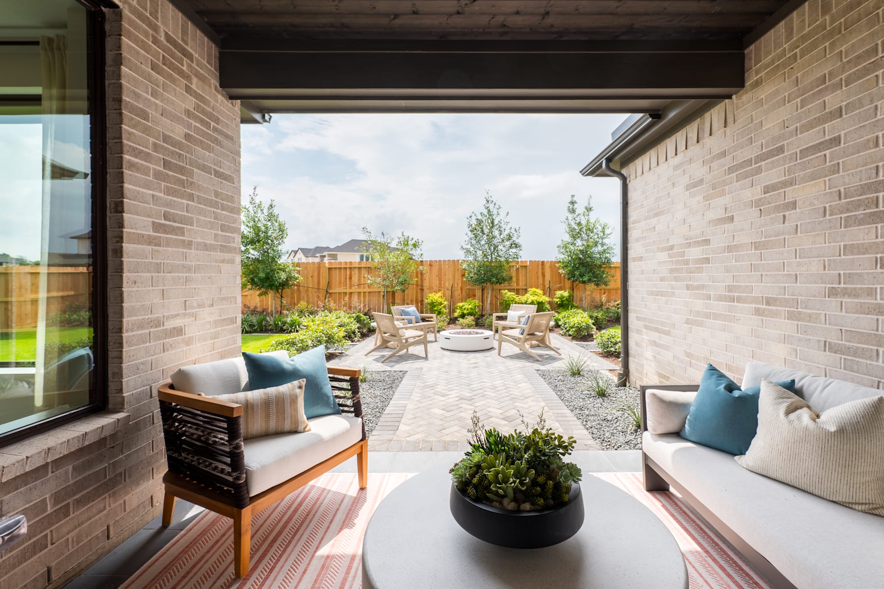 A cozy outdoor living space with comfortable seating, a paved walkway, and lush greenery surrounding the area, creating a serene and inviting atmosphere.