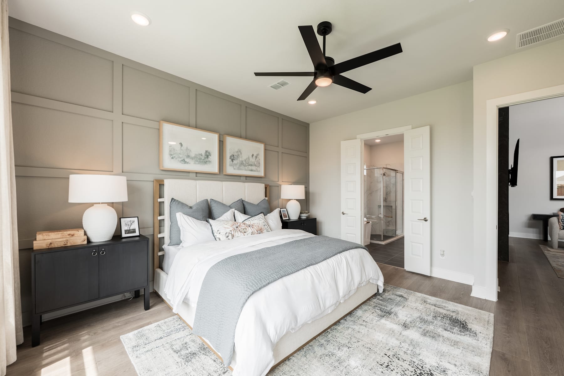 A cozy and well-designed bedroom with a large bed, gray and white color scheme, and a ceiling fan providing a comfortable atmosphere.