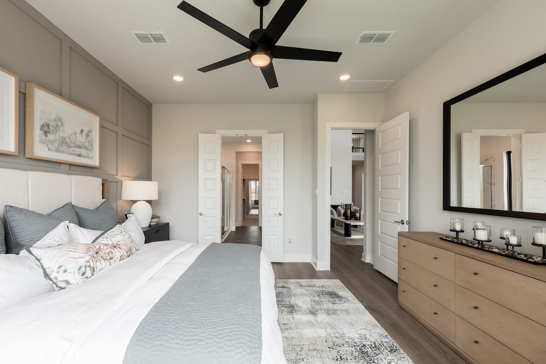 A spacious and well-designed bedroom with a large bed, a ceiling fan, and a dresser in the background, creating a cozy and inviting atmosphere.