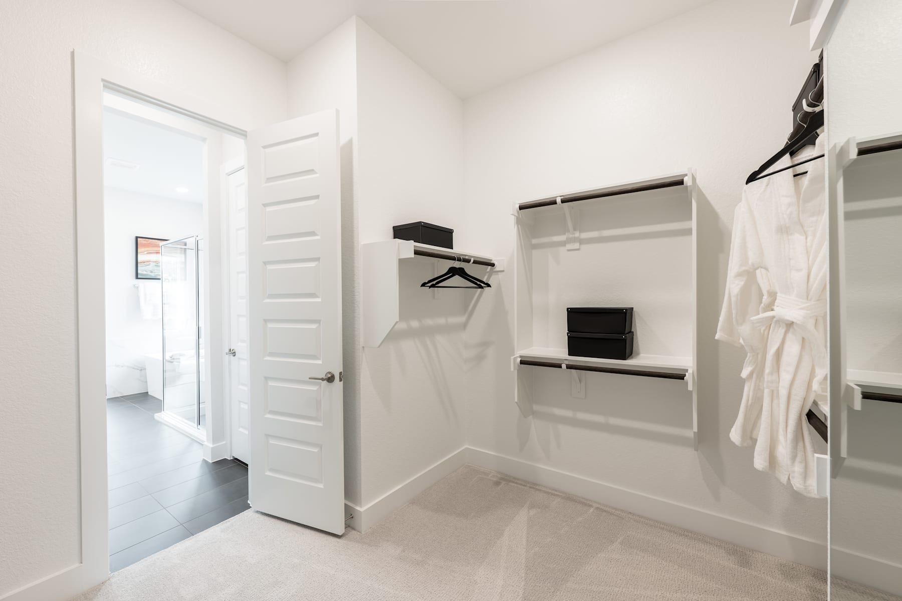 A bright, minimalist closet space with white walls, a hanging rod, and shelves for storage.