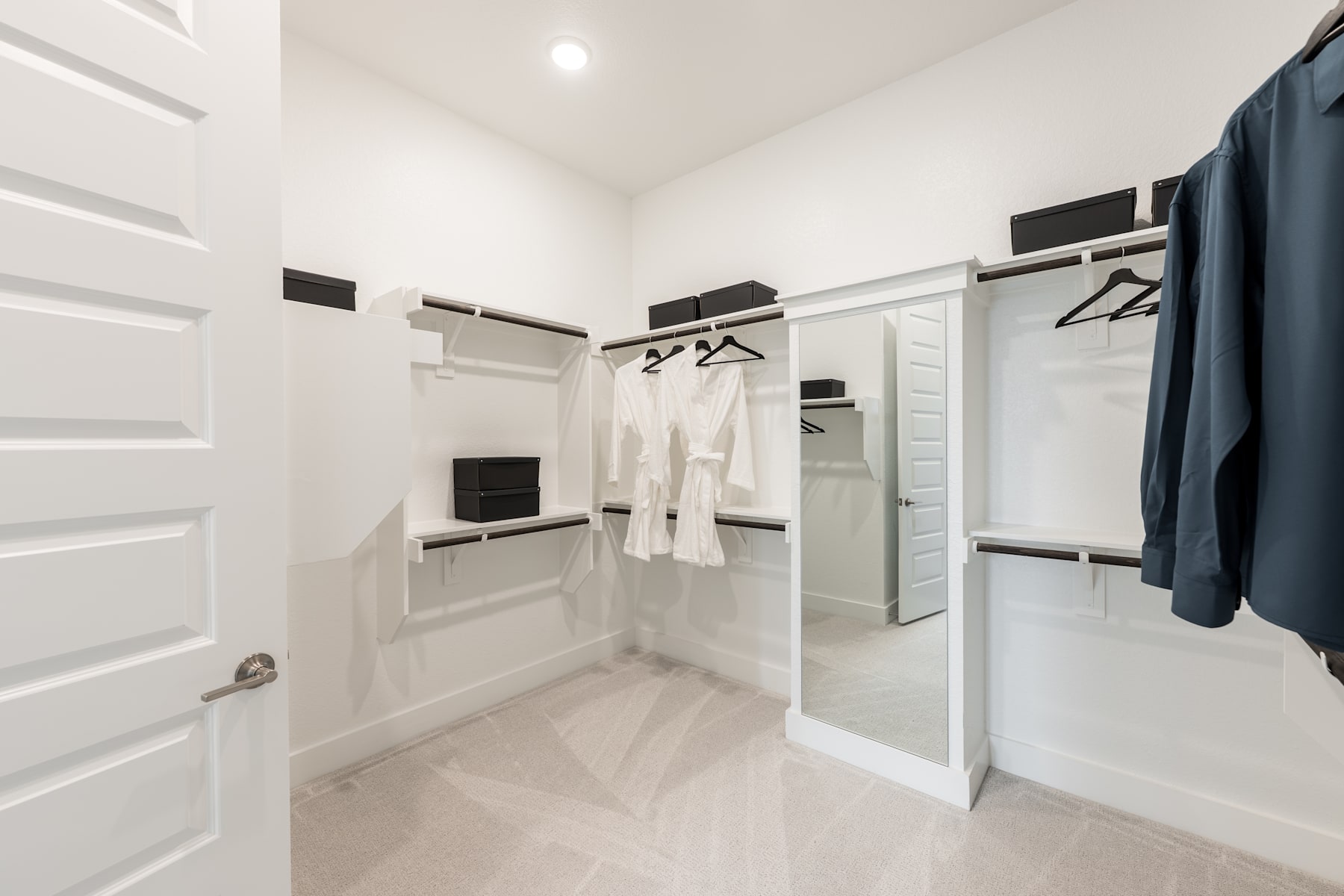 A bright, minimalist walk-in closet with white walls, hanging clothes, and a wooden floor.