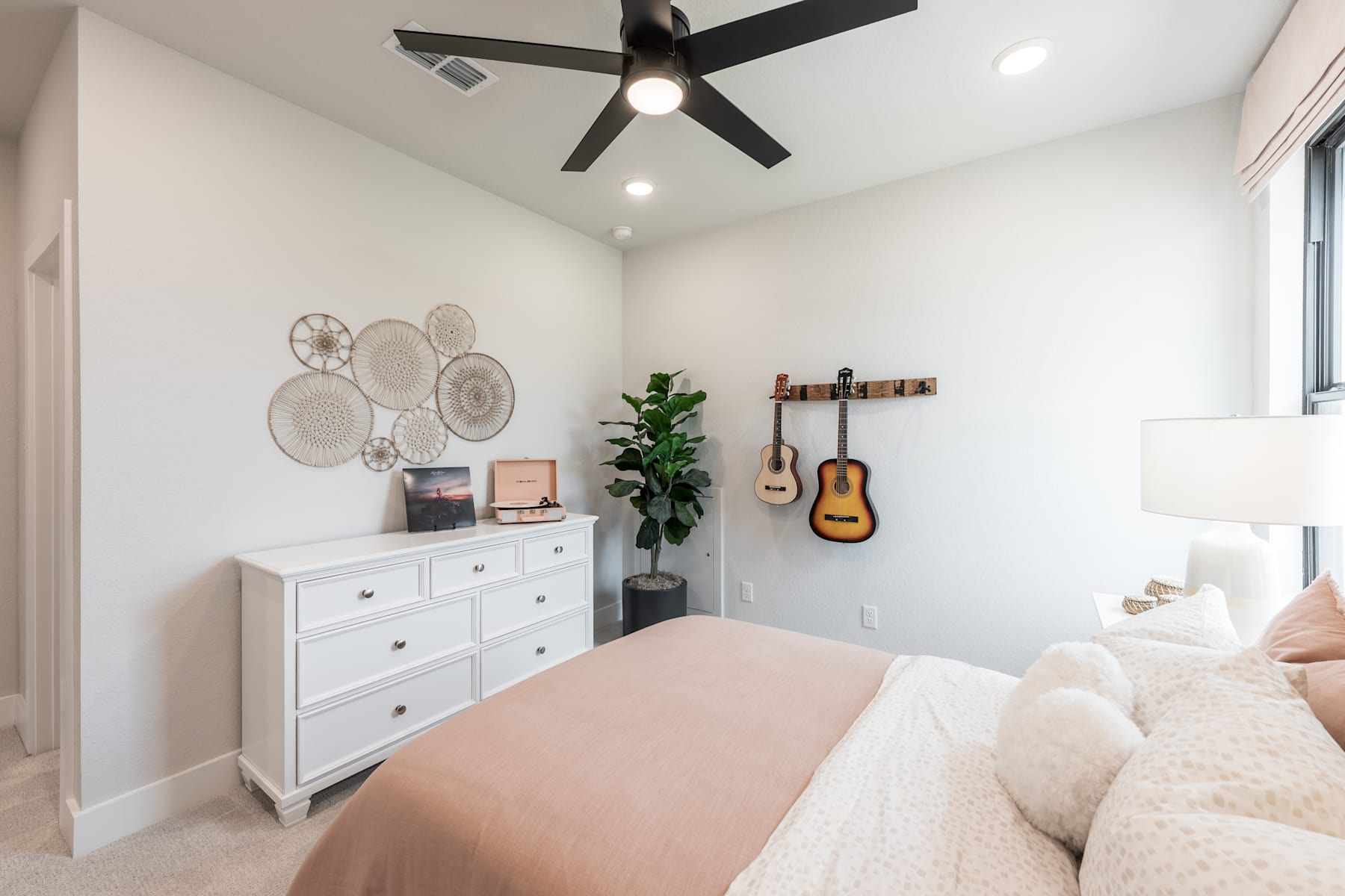 A cozy and well-decorated bedroom with a white dresser, a guitar hanging on the wall, and a ceiling fan providing a comfortable atmosphere.