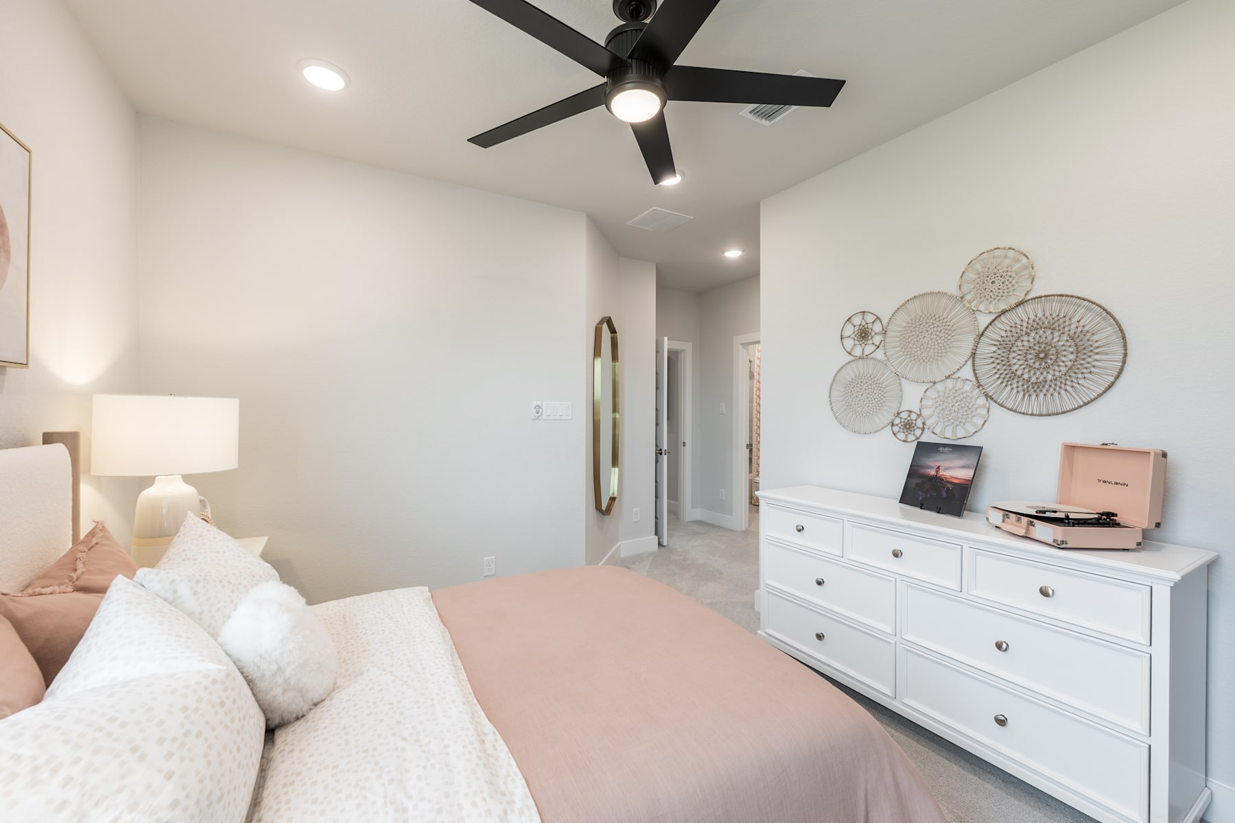 A cozy and modern bedroom with a white dresser, decorative wall art, and a ceiling fan, creating a warm and inviting atmosphere.