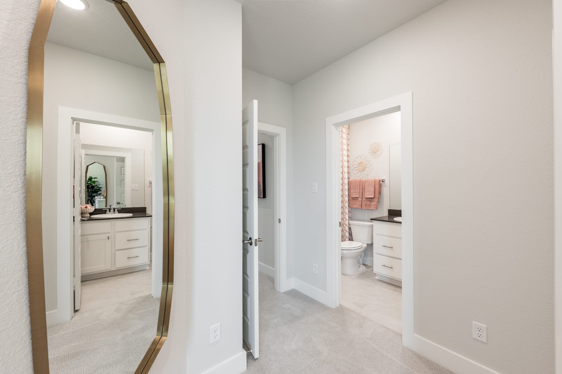 A bright and airy hallway with a large mirror on the wall, leading to two open doorways revealing a bathroom and another room.