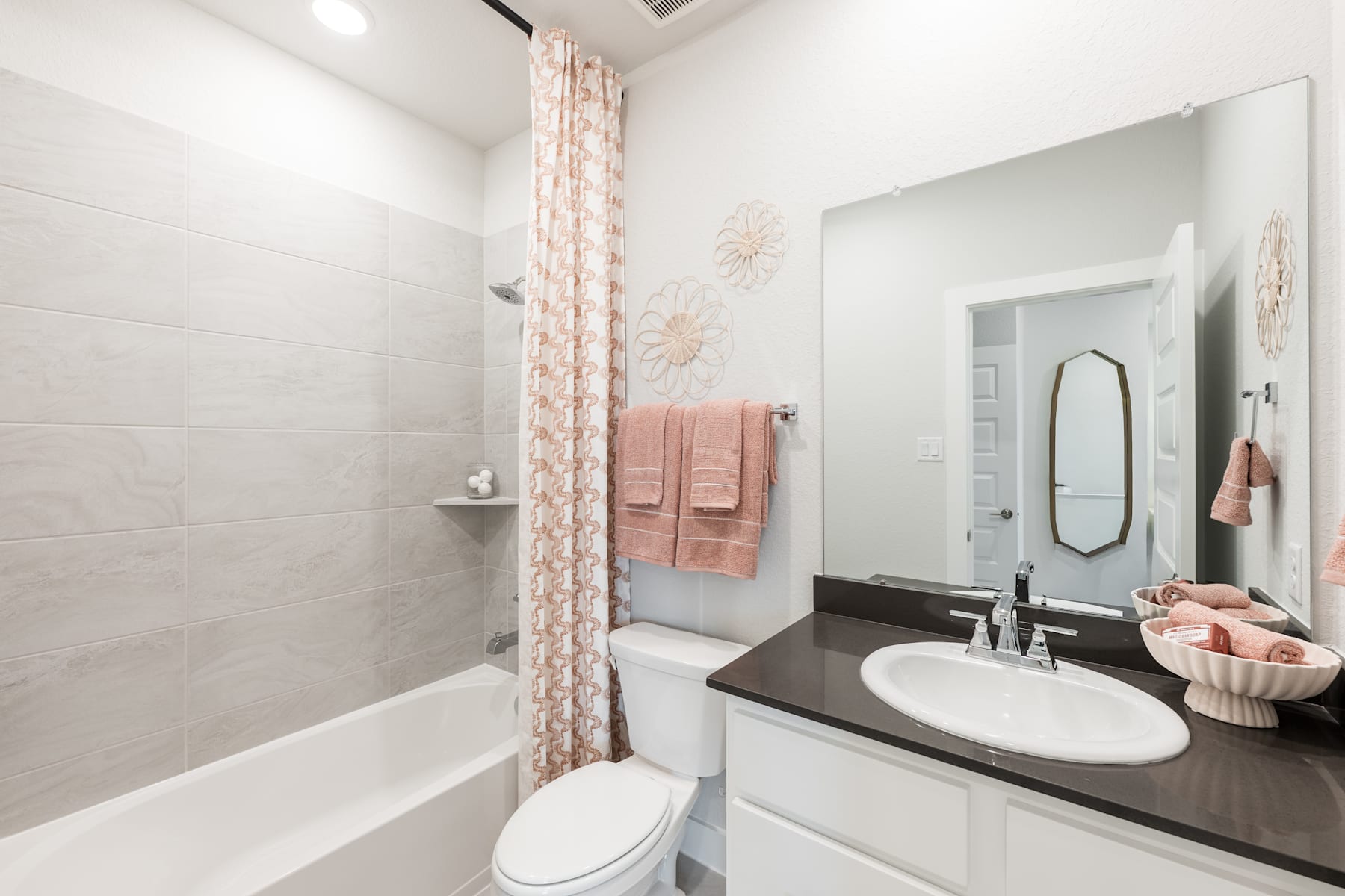 A modern, well-lit bathroom with a white vanity, a large mirror, and a patterned curtain hanging over the bathtub.