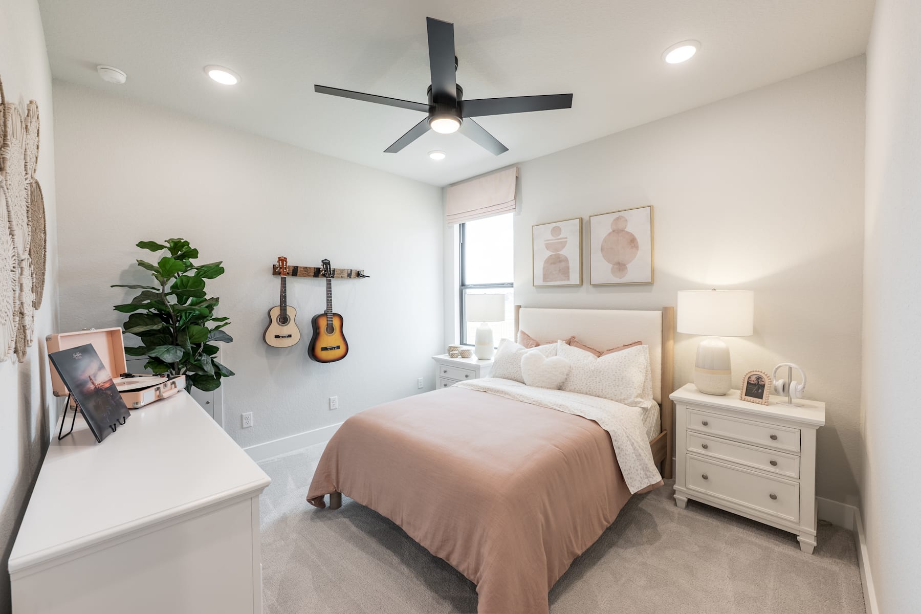 A cozy and well-decorated bedroom with a ceiling fan, a bed with a pink comforter, a guitar on the wall, and a potted plant in the corner.