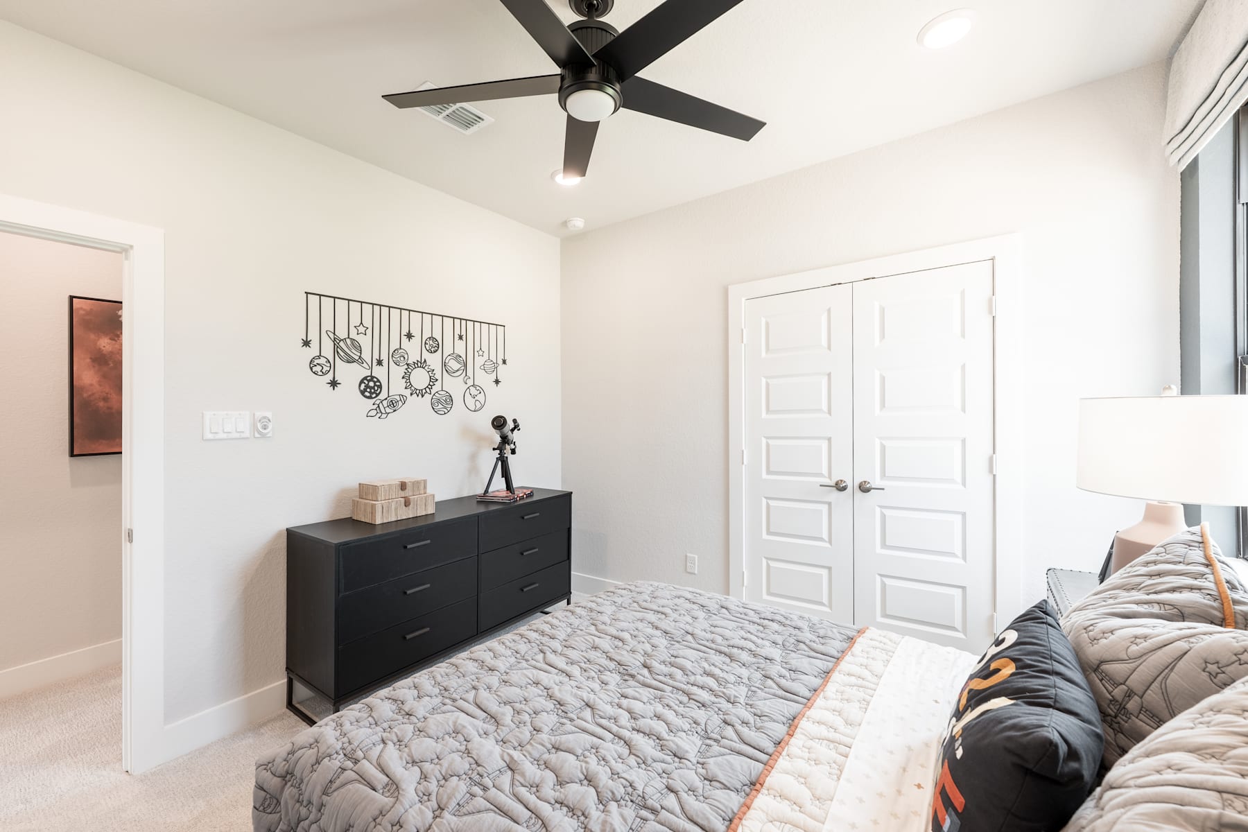 A cozy and well-furnished bedroom with a ceiling fan, a black dresser, and various decorative items on the walls.