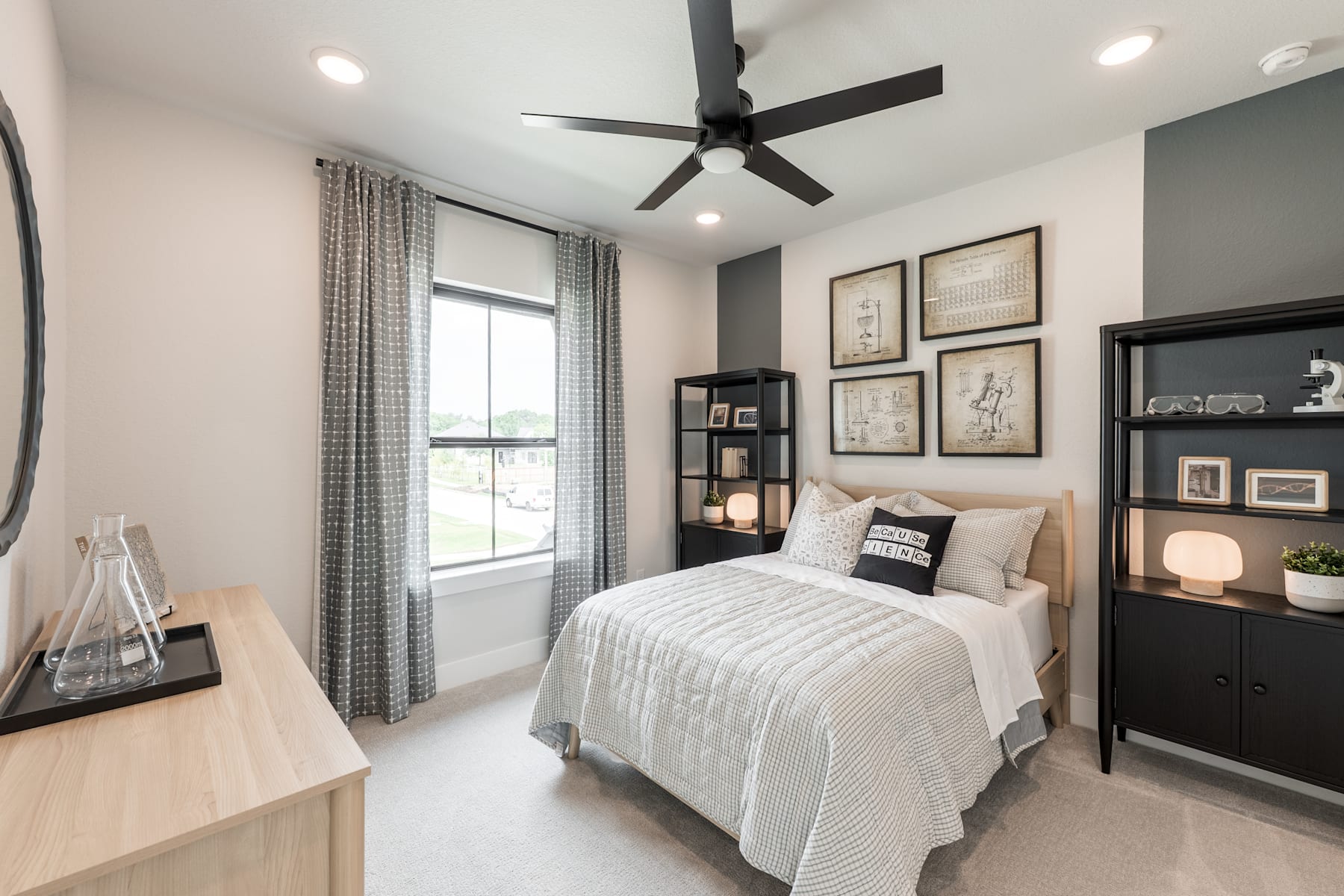 A cozy and well-designed bedroom with a large window, a ceiling fan, and a variety of framed artwork and decor elements on the walls, creating a warm and inviting atmosphere.