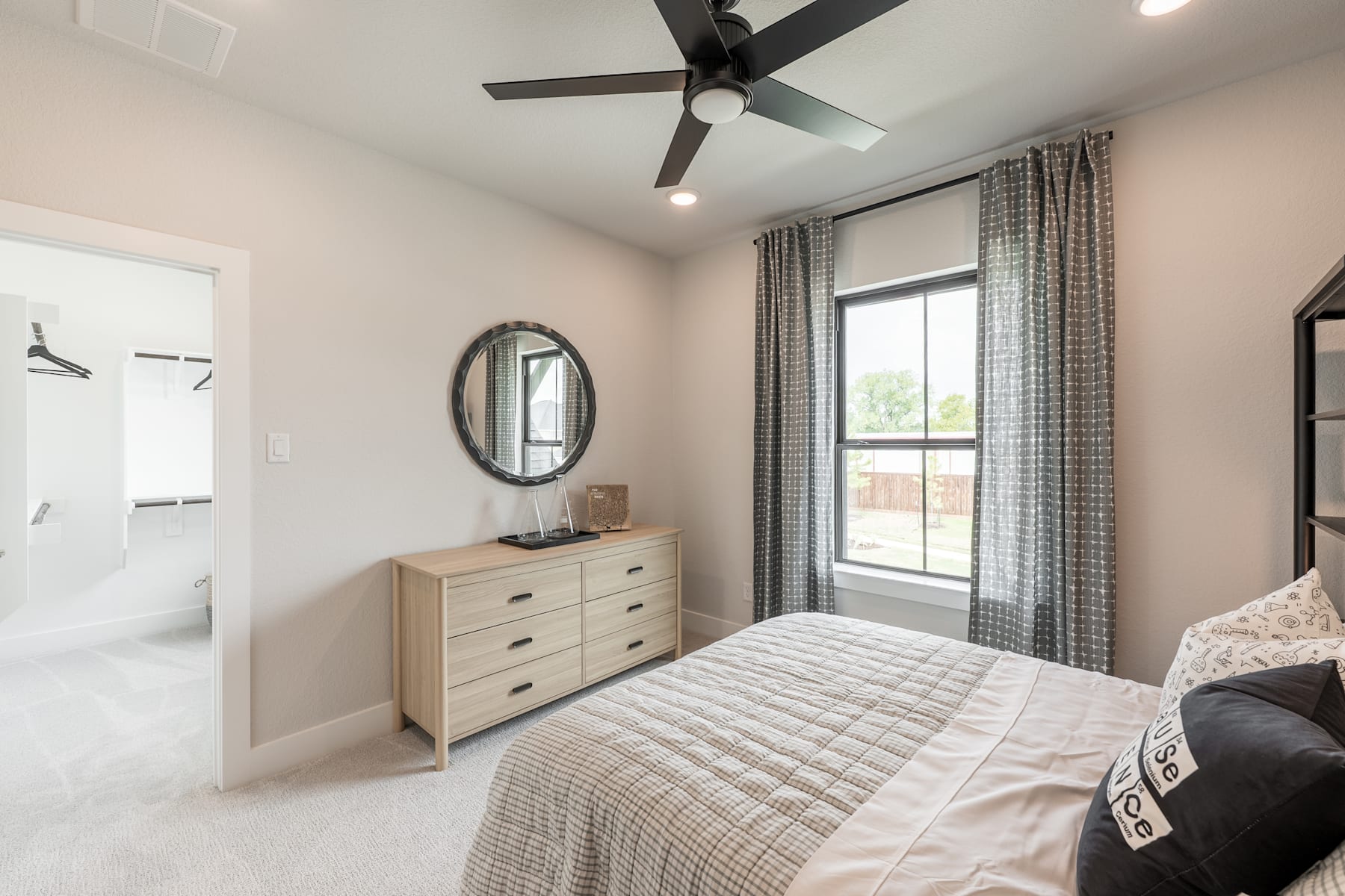 A cozy and well-furnished bedroom with a large bed, a dresser, and a ceiling fan, set against a backdrop of a window overlooking an outdoor scene.