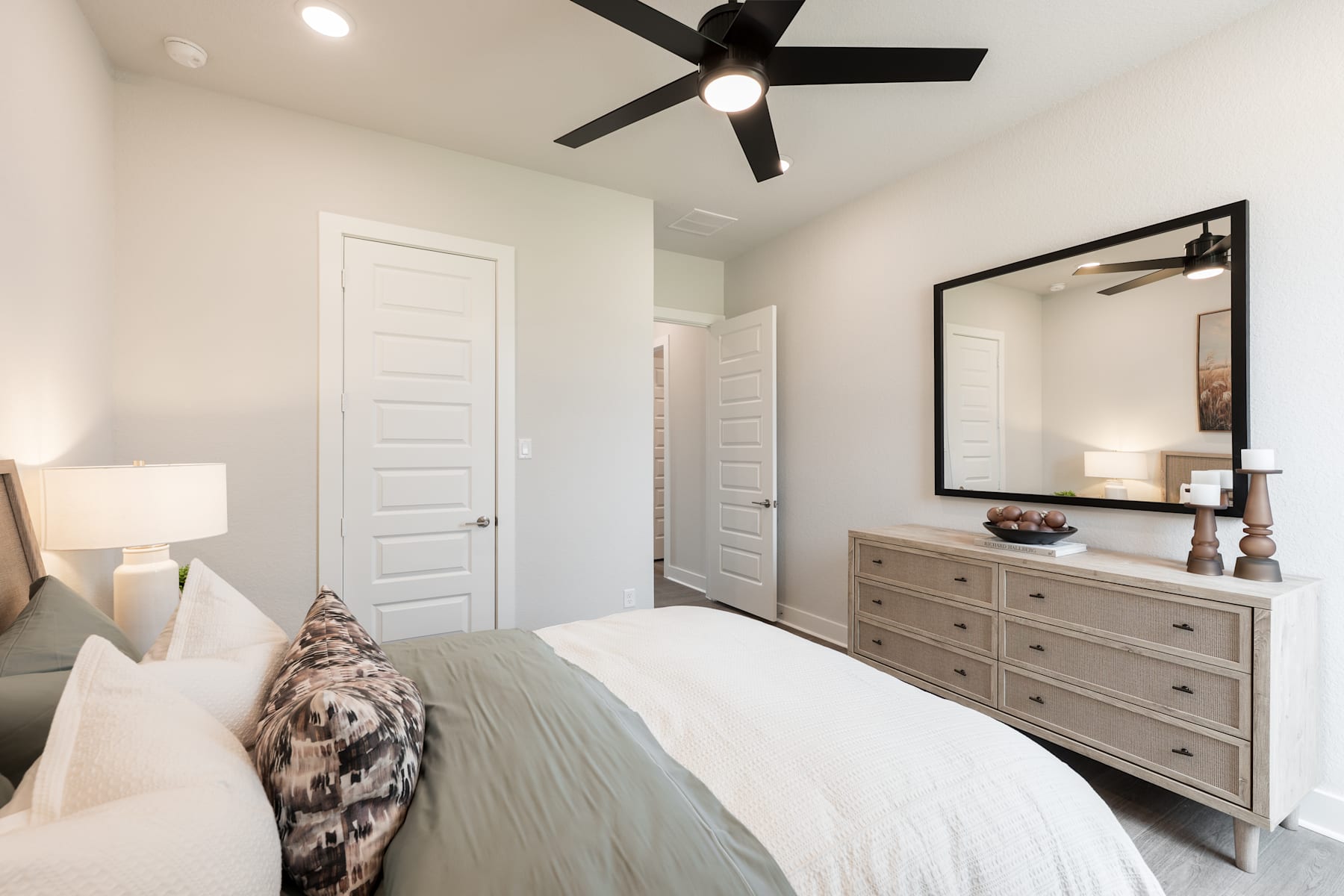 A cozy and well-furnished bedroom with a large bed, a dresser, and a ceiling fan, set against a neutral color palette and clean, modern design.