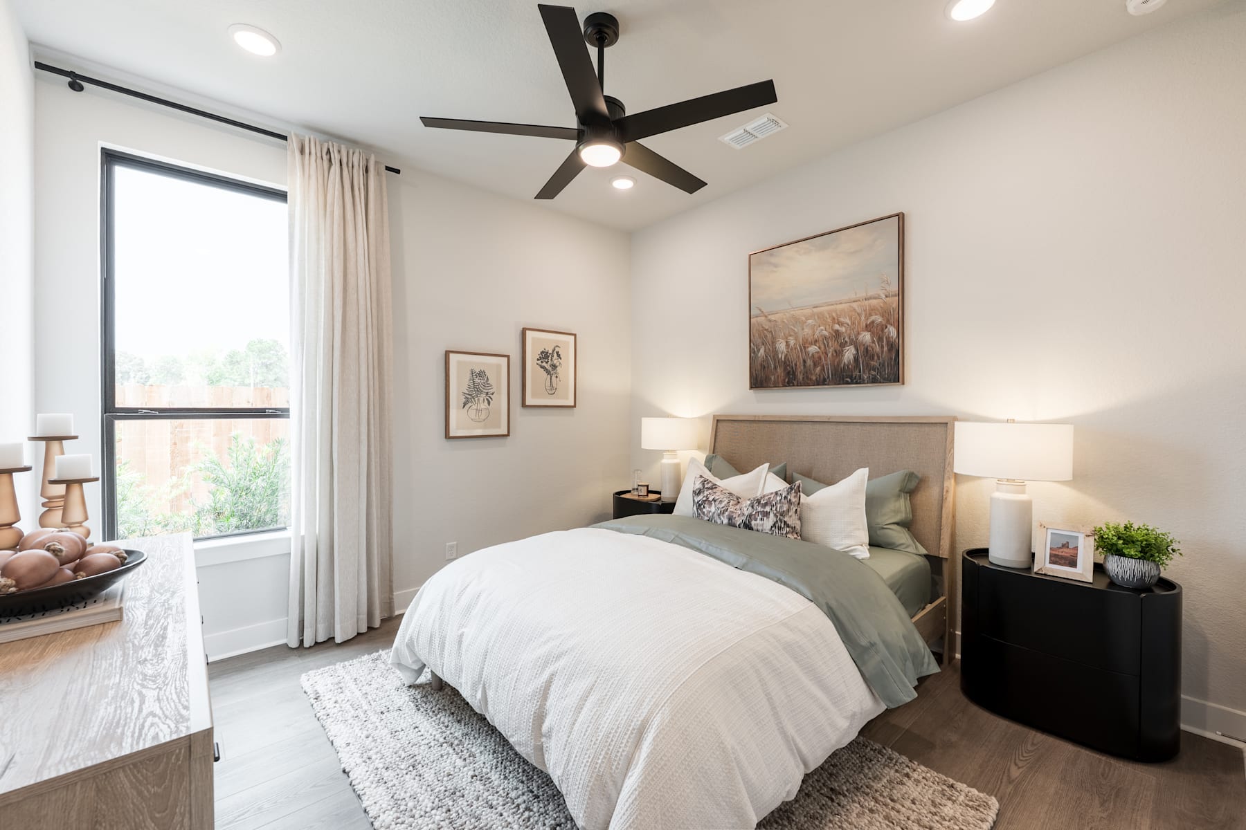 A cozy and well-designed bedroom with a large bed, a ceiling fan, and various decorative elements, including artwork and potted plants, creating a warm and inviting atmosphere.
