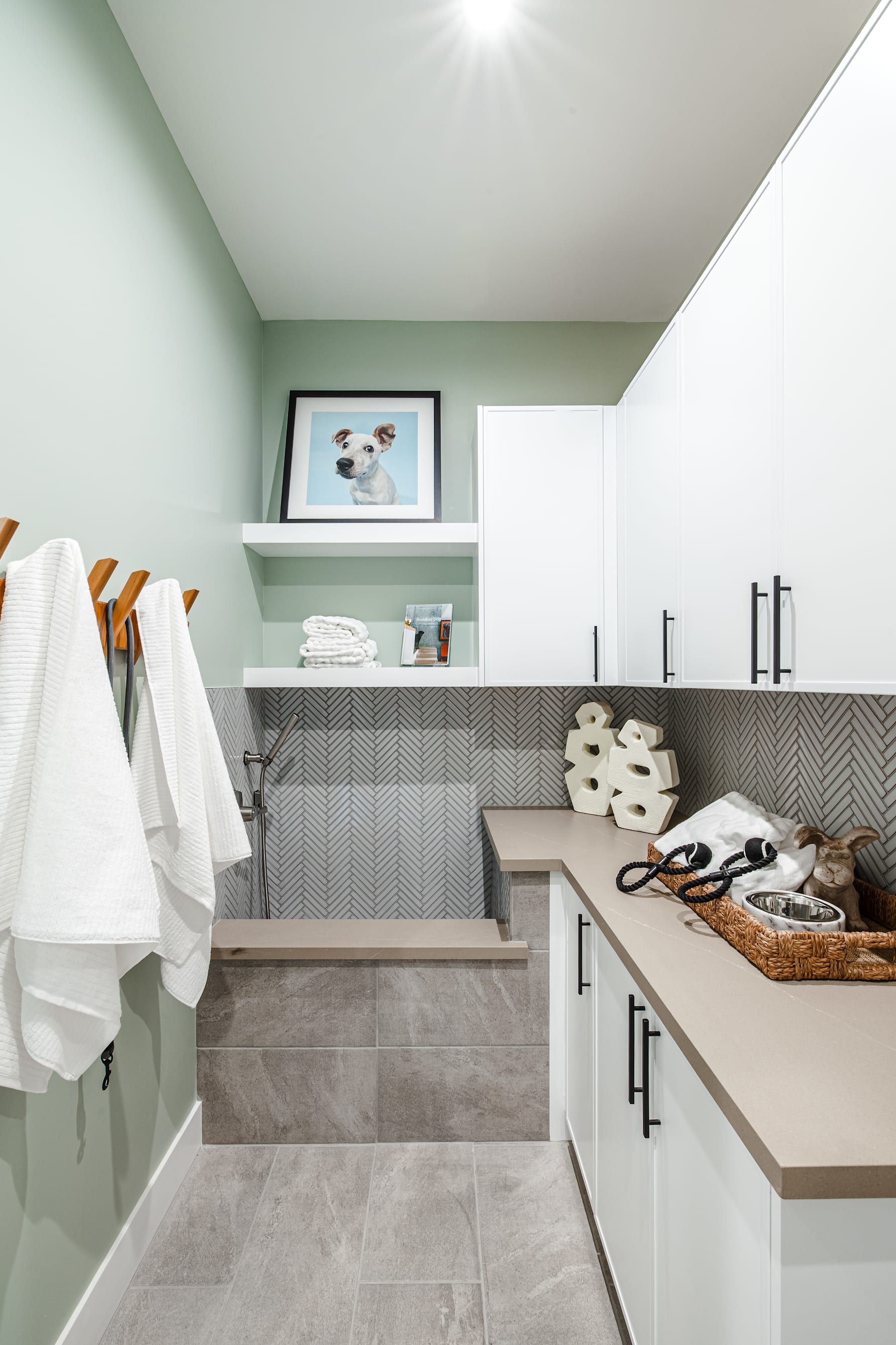 A modern and minimalist bathroom with light green walls, gray tile flooring, and a wooden vanity with various bathroom accessories and towels.