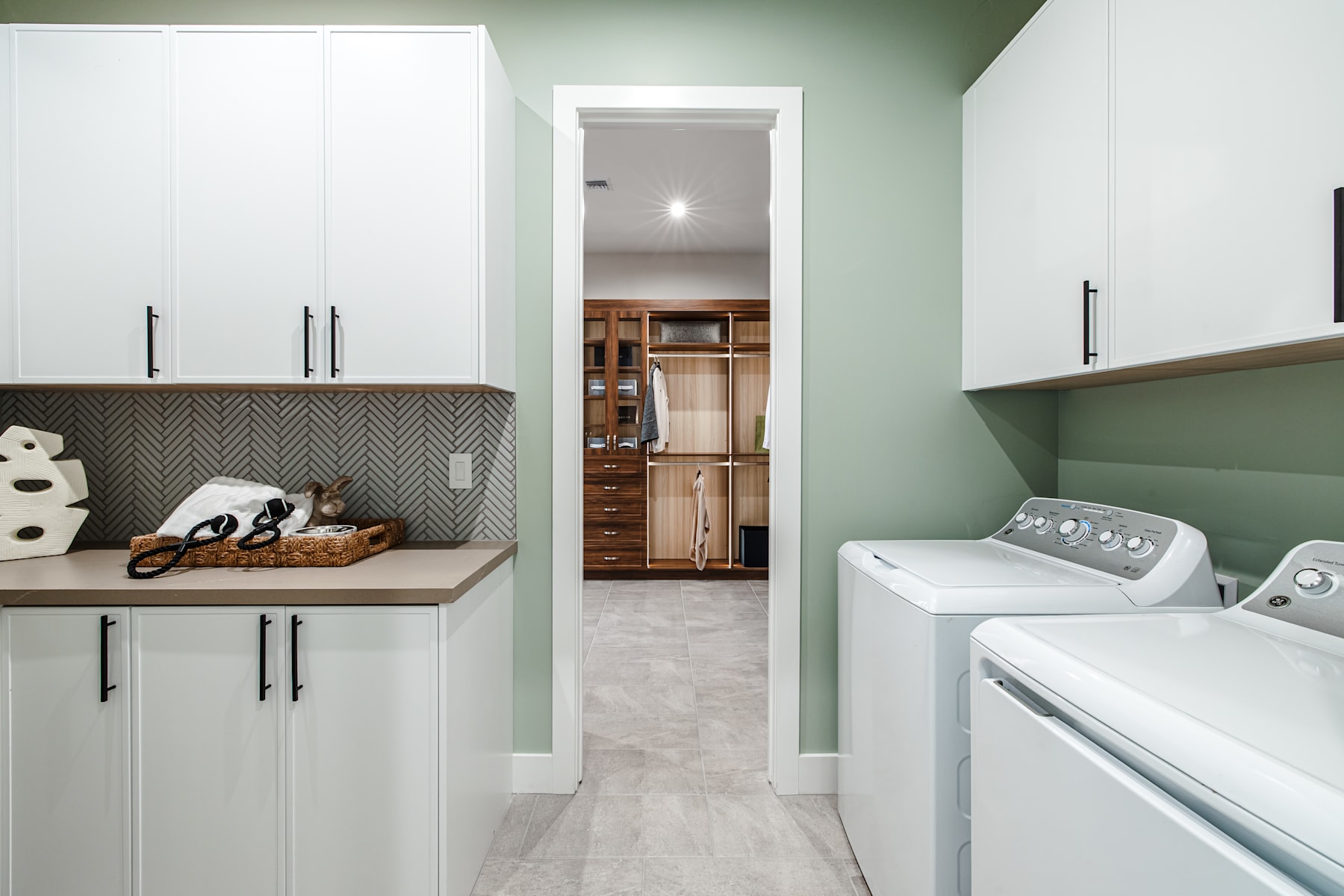 A modern and well-organized laundry room with white cabinets, a wooden countertop, and a washer and dryer visible in the background.