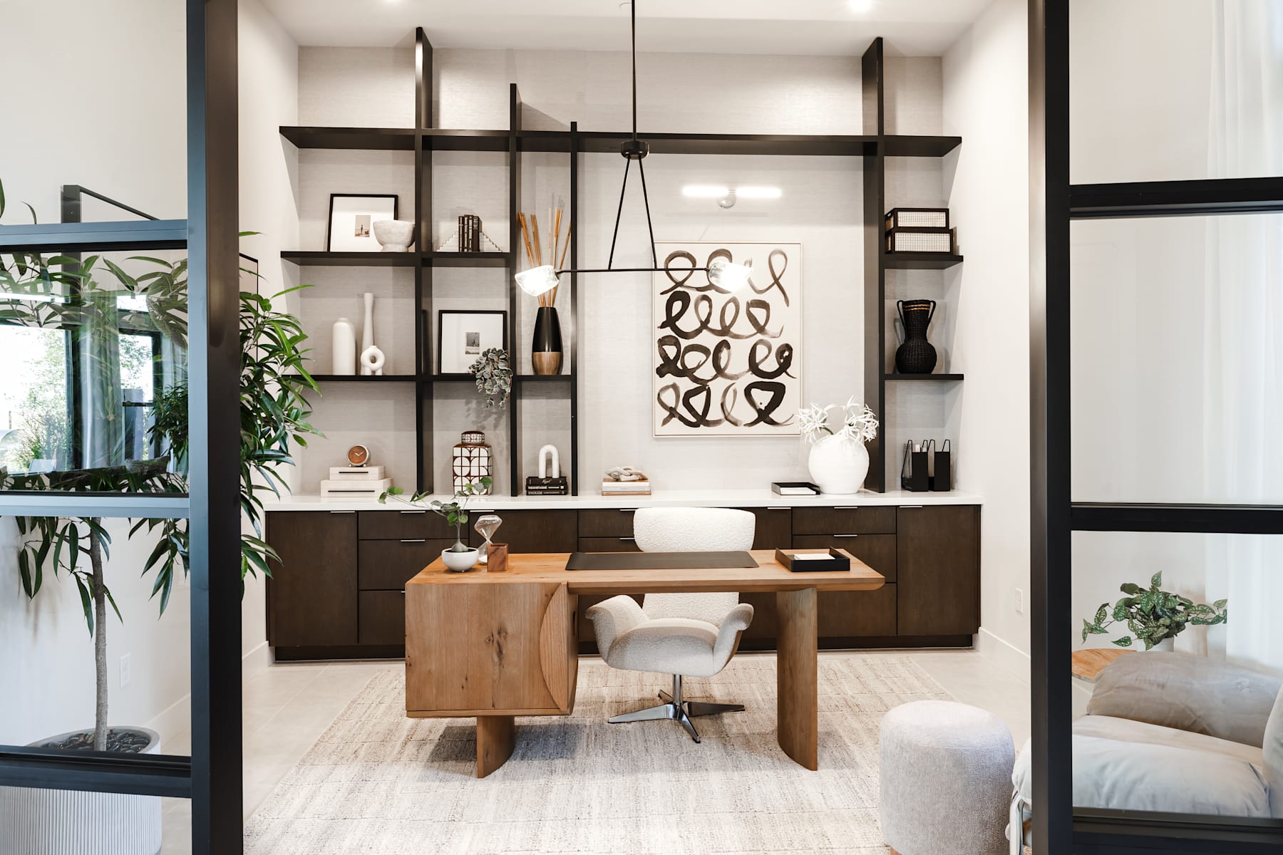 A modern and minimalist home office space with wooden furniture, shelves displaying decorative items, and a large window providing natural light.