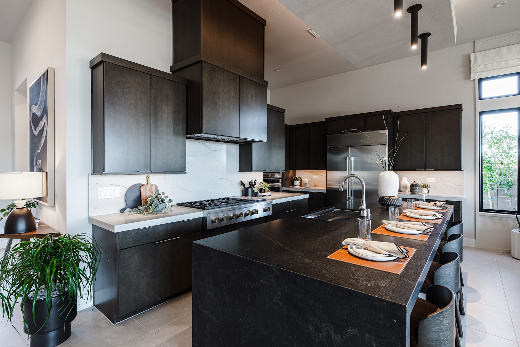 A modern, sleek kitchen with dark cabinets, a large countertop, and various kitchen appliances and decor elements.