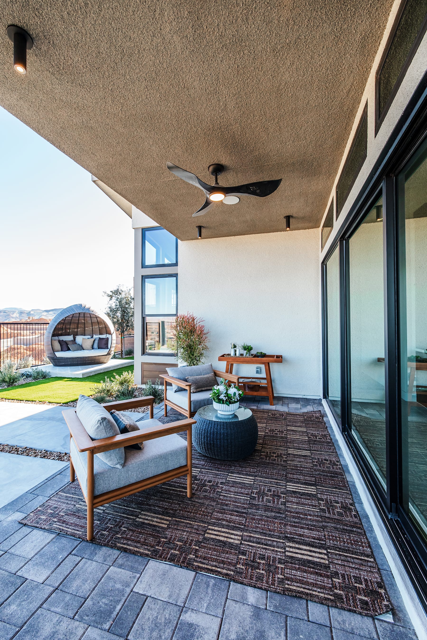 A cozy outdoor patio area with comfortable seating, a ceiling fan, and a view of the surrounding landscape through large windows.