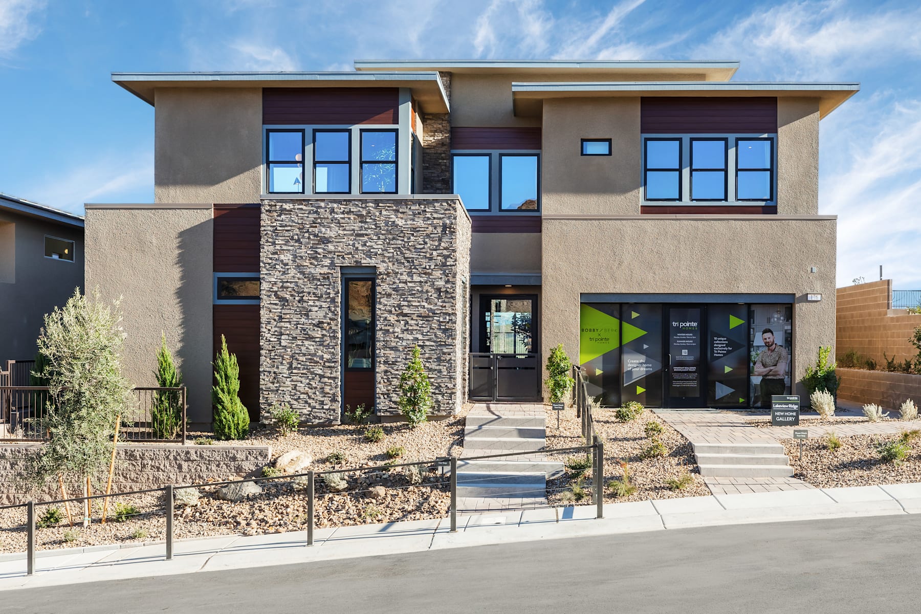 A modern, two-story residential building with a stone facade, large windows, and a landscaped front yard with a walkway leading to the entrance.