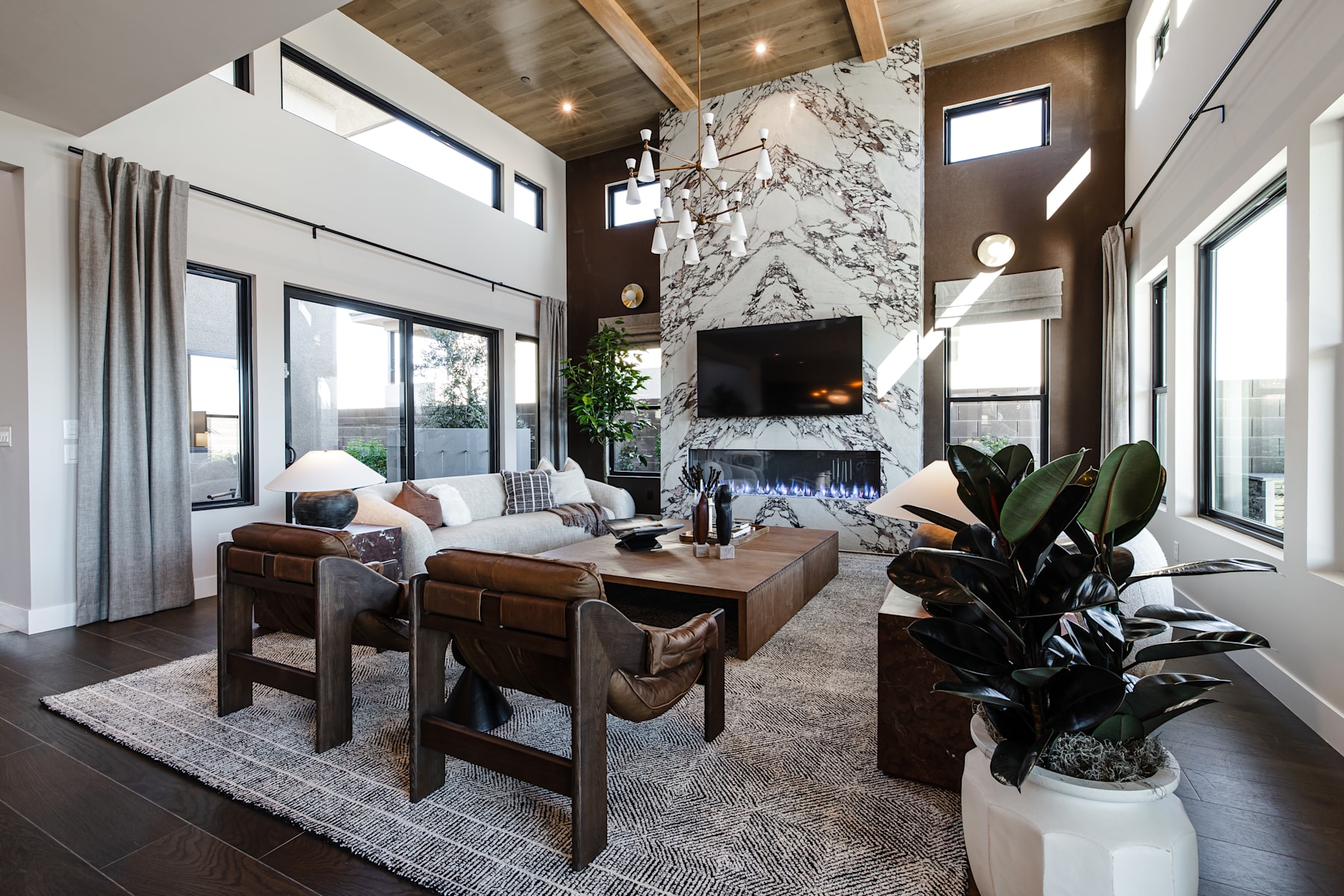 A spacious and modern living room with a large marble fireplace, comfortable leather furniture, and a lush indoor plant, all bathed in natural light from the large windows.