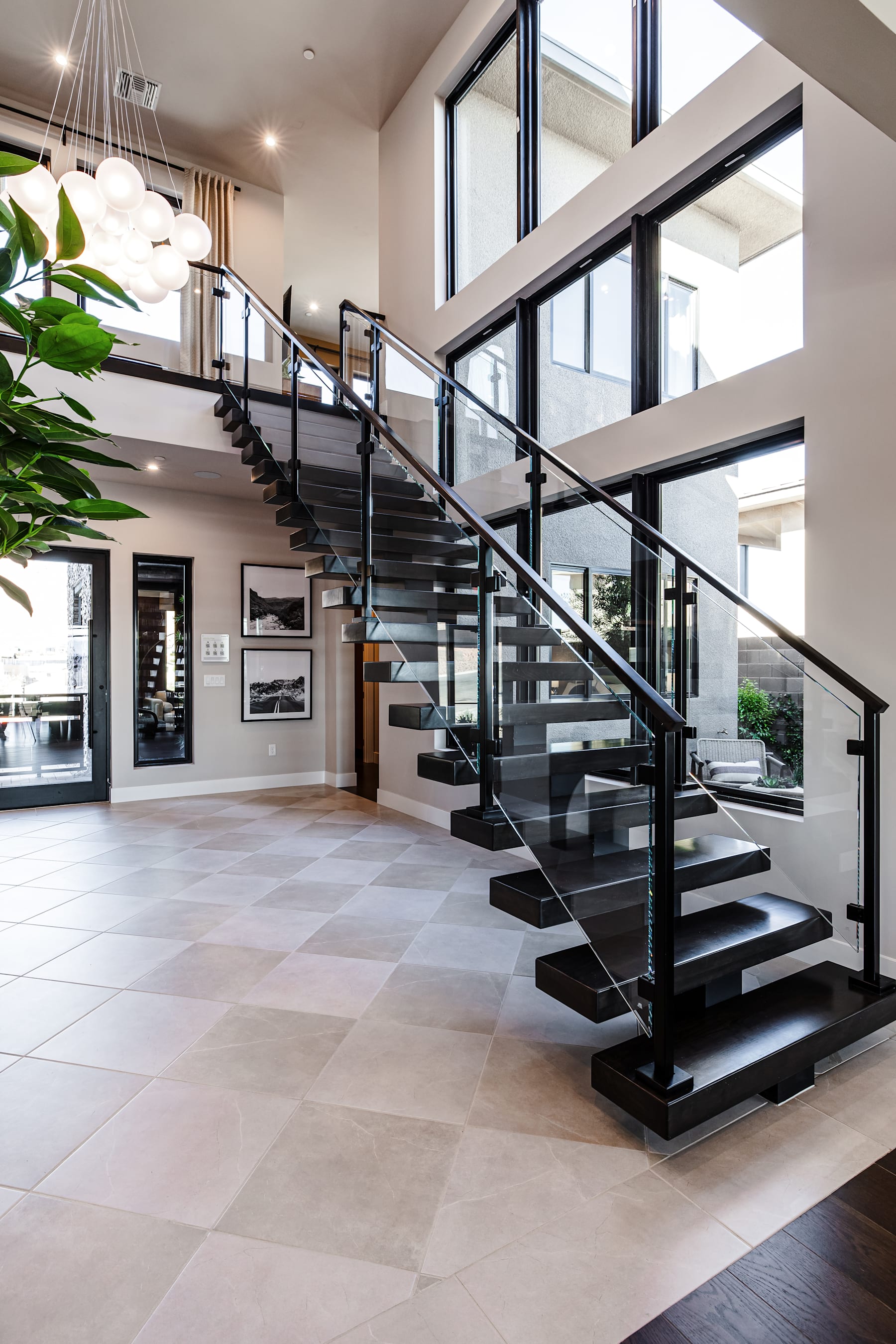 A modern and spacious entryway with a grand staircase featuring sleek black metal railings and steps, surrounded by large windows that allow natural light to flood the space, and a potted plant adding a touch of greenery to the minimalist decor.