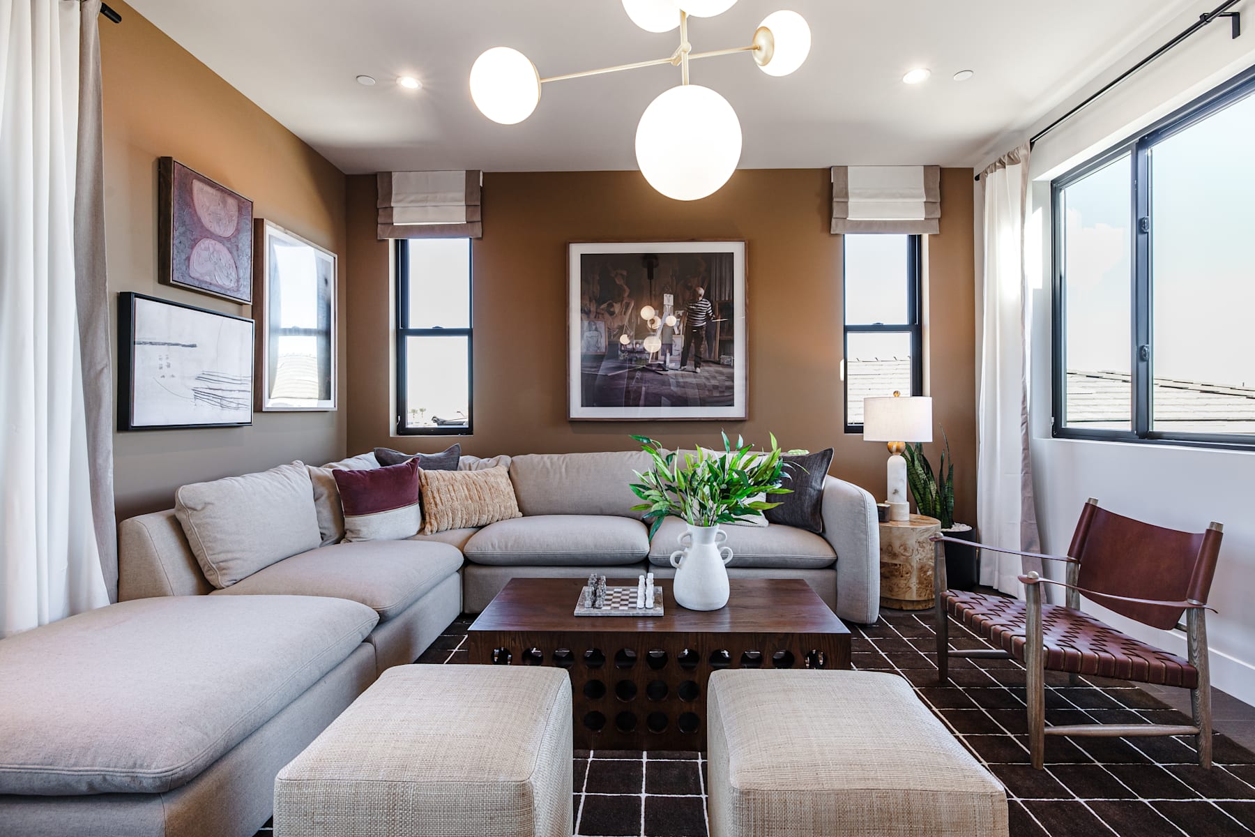 A cozy and stylish living room with a plush gray sectional sofa, a patterned area rug, and a large framed artwork on the wall, complemented by modern pendant lighting fixtures.