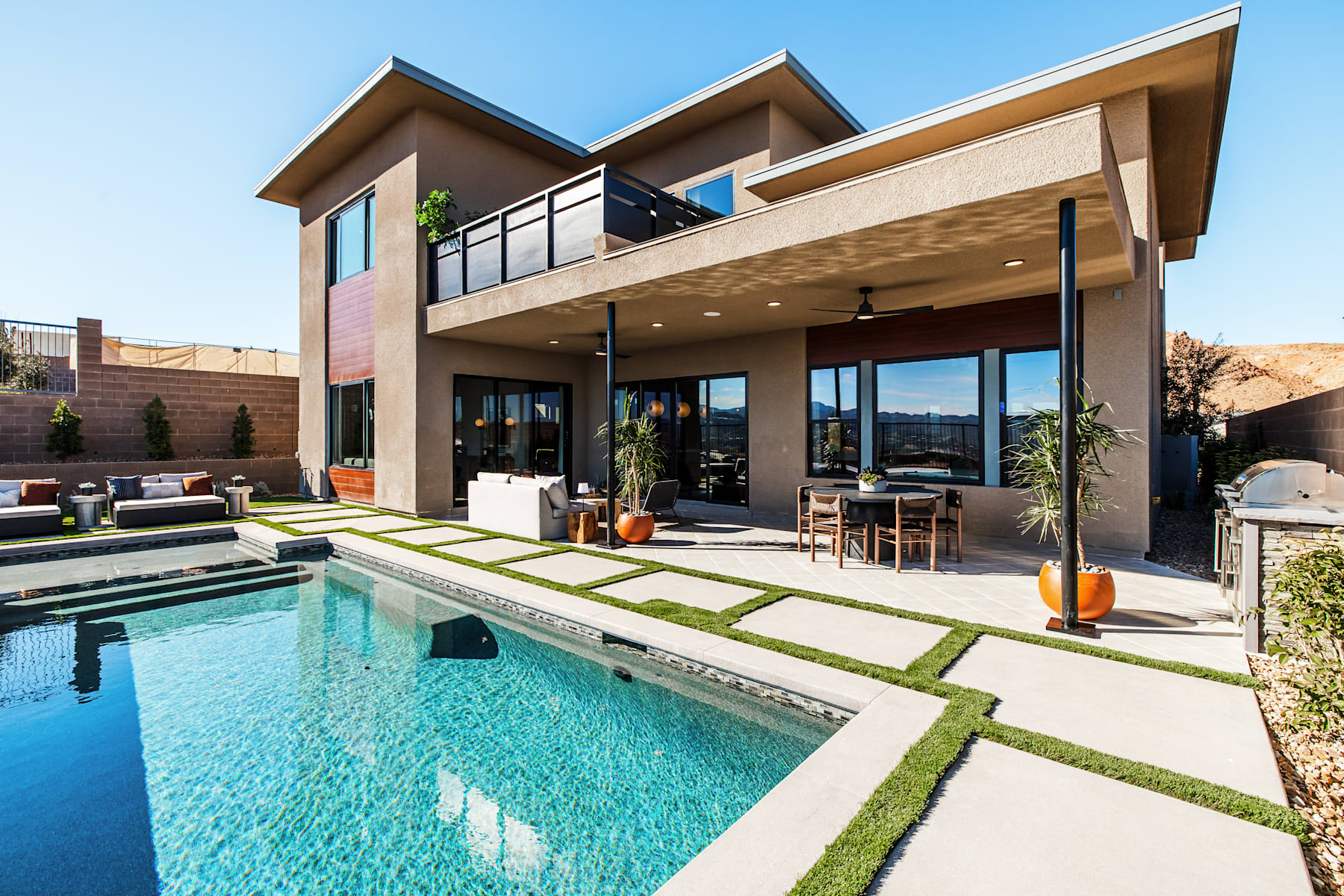 A modern, two-story house with a pool in the foreground, surrounded by a lush, landscaped yard and a clear blue sky in the background.