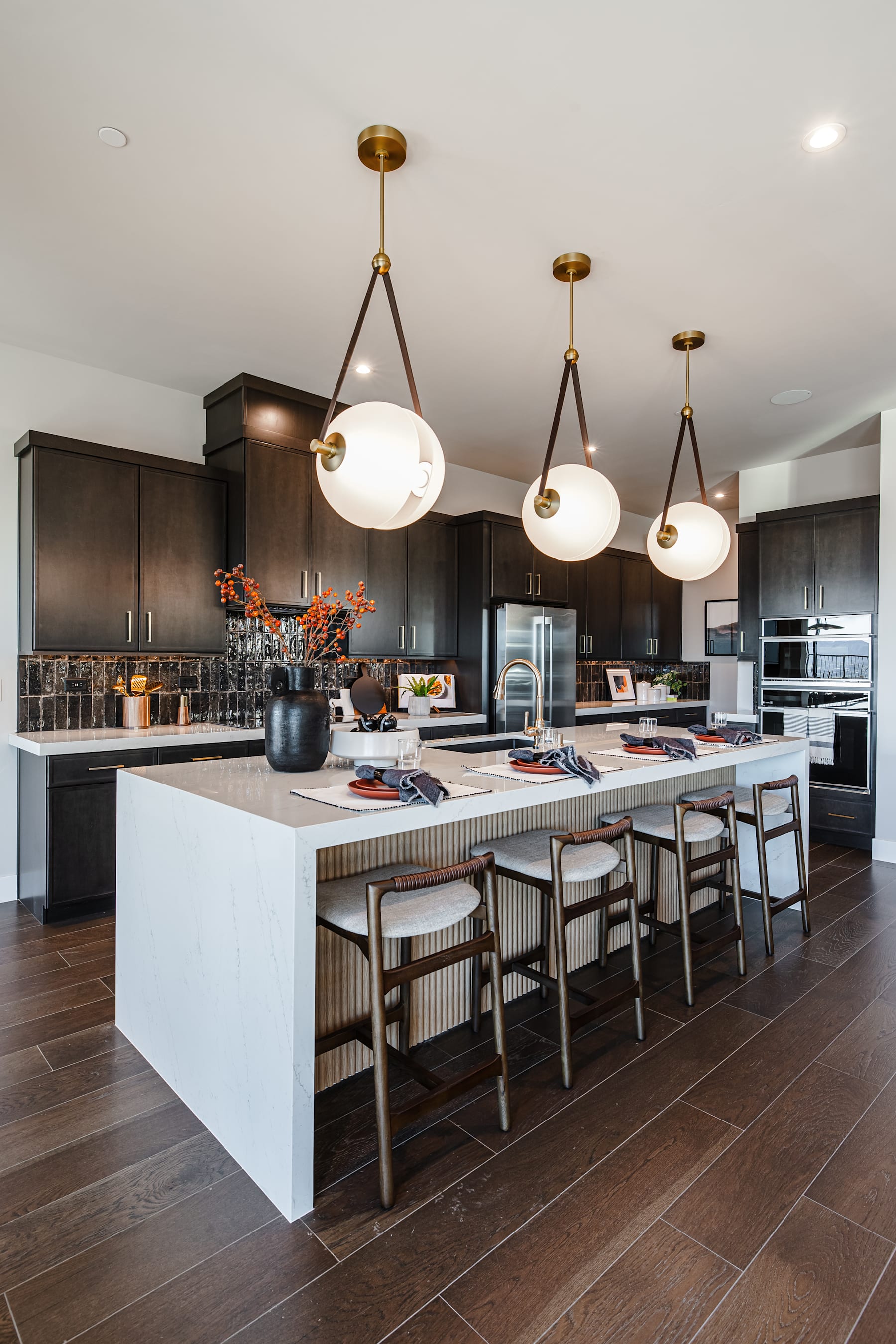 A modern and spacious kitchen with dark wood cabinets, a large white island with bar stools, and three pendant lights hanging above the island.