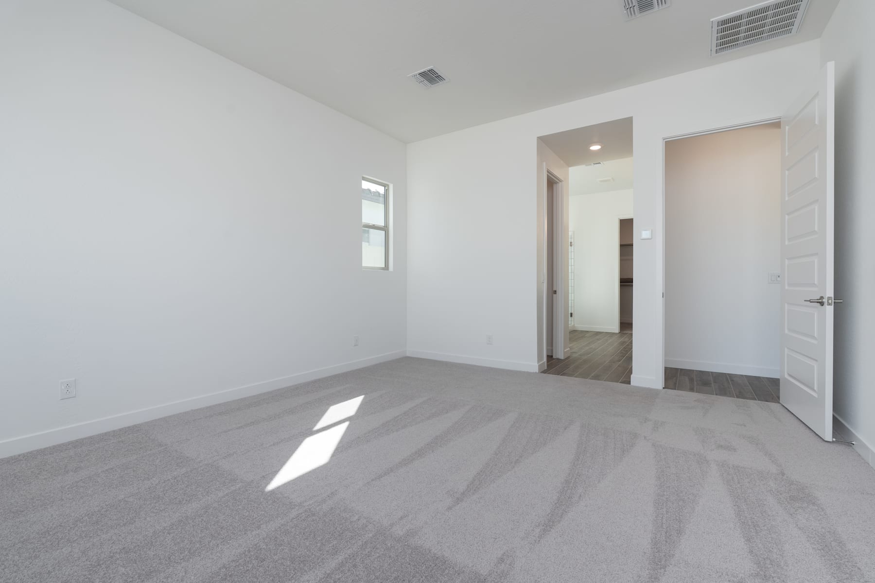 A spacious, minimalist room with white walls, a grey hardwood floor, and a doorway leading to another room.