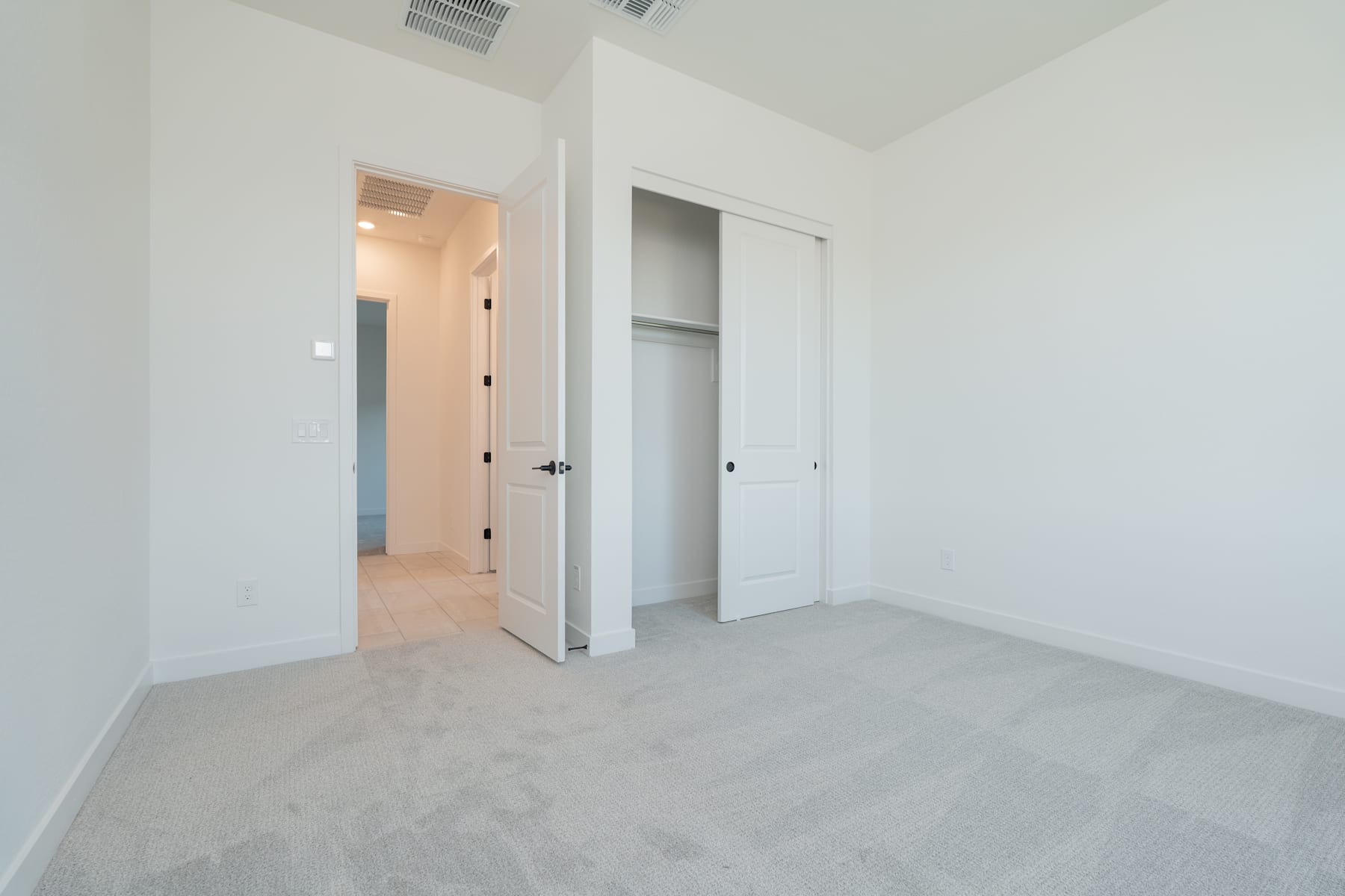 A spacious, minimalist room with white walls, a closet, and an open doorway leading to another room.