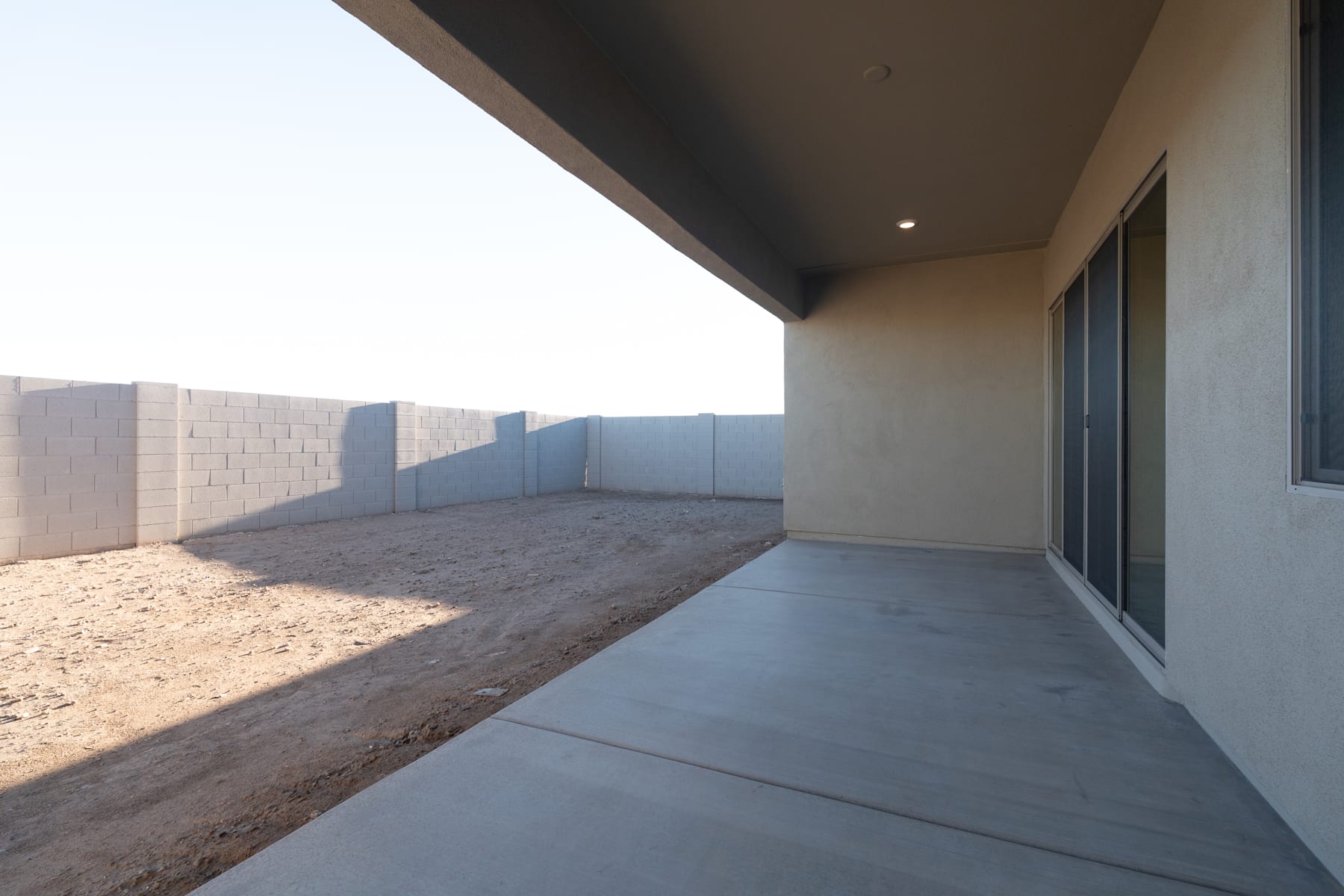 A concrete walkway leads to a partially visible building, with a wall and fencing visible in the background, creating a sense of enclosure and privacy.