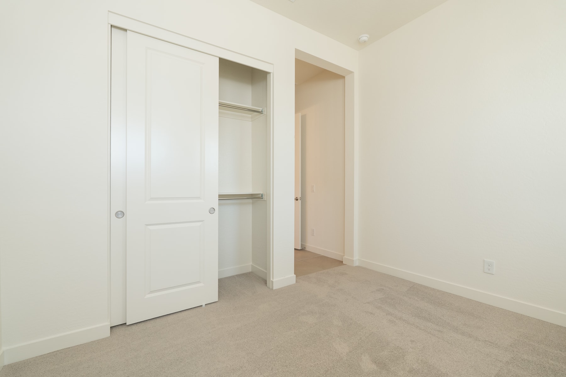 A spacious, well-lit room with a closet and an open doorway leading to another room, featuring a neutral color scheme and hardwood flooring.