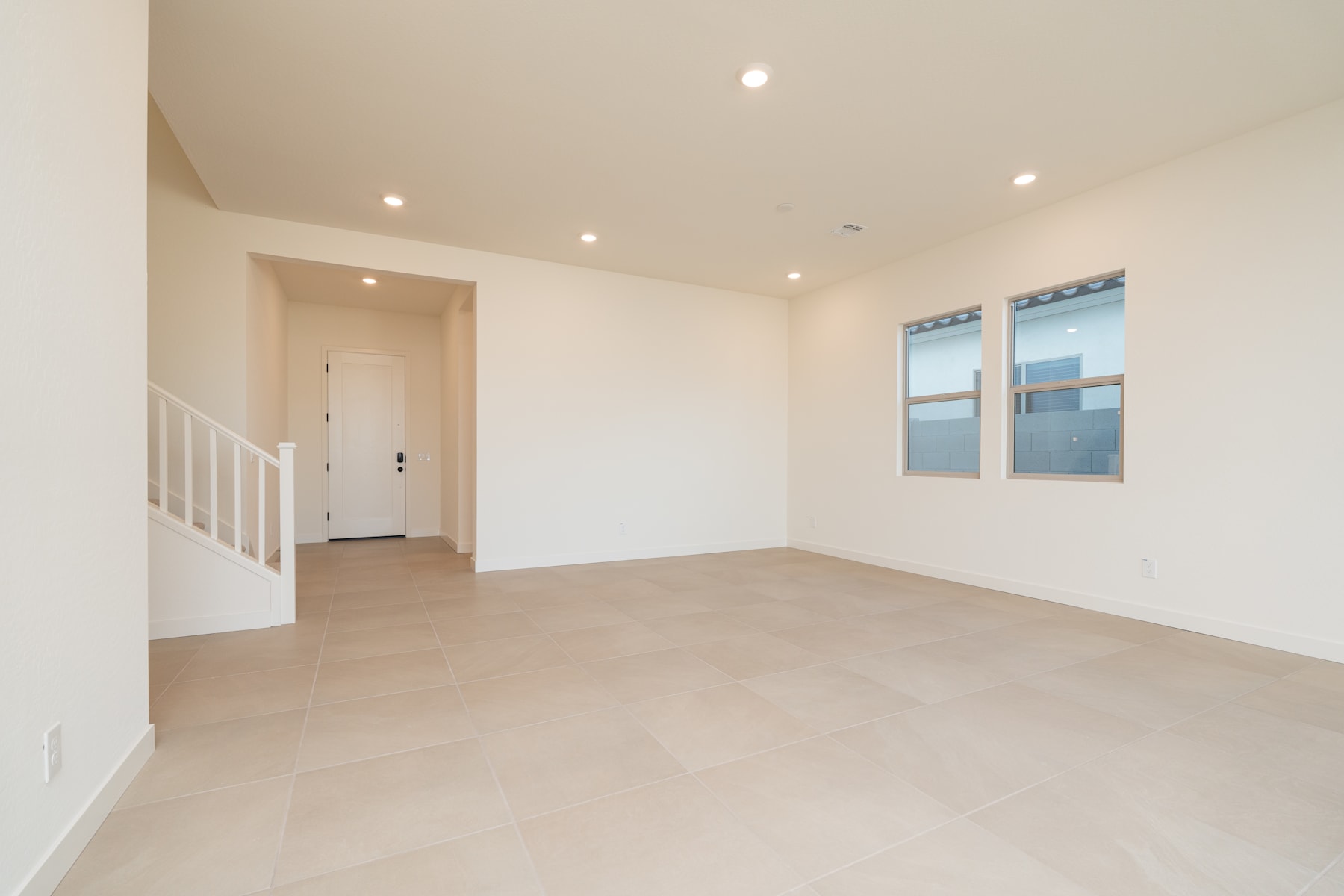 A spacious, minimalist room with white walls, a hardwood floor, and recessed lighting, featuring a doorway leading to another area.