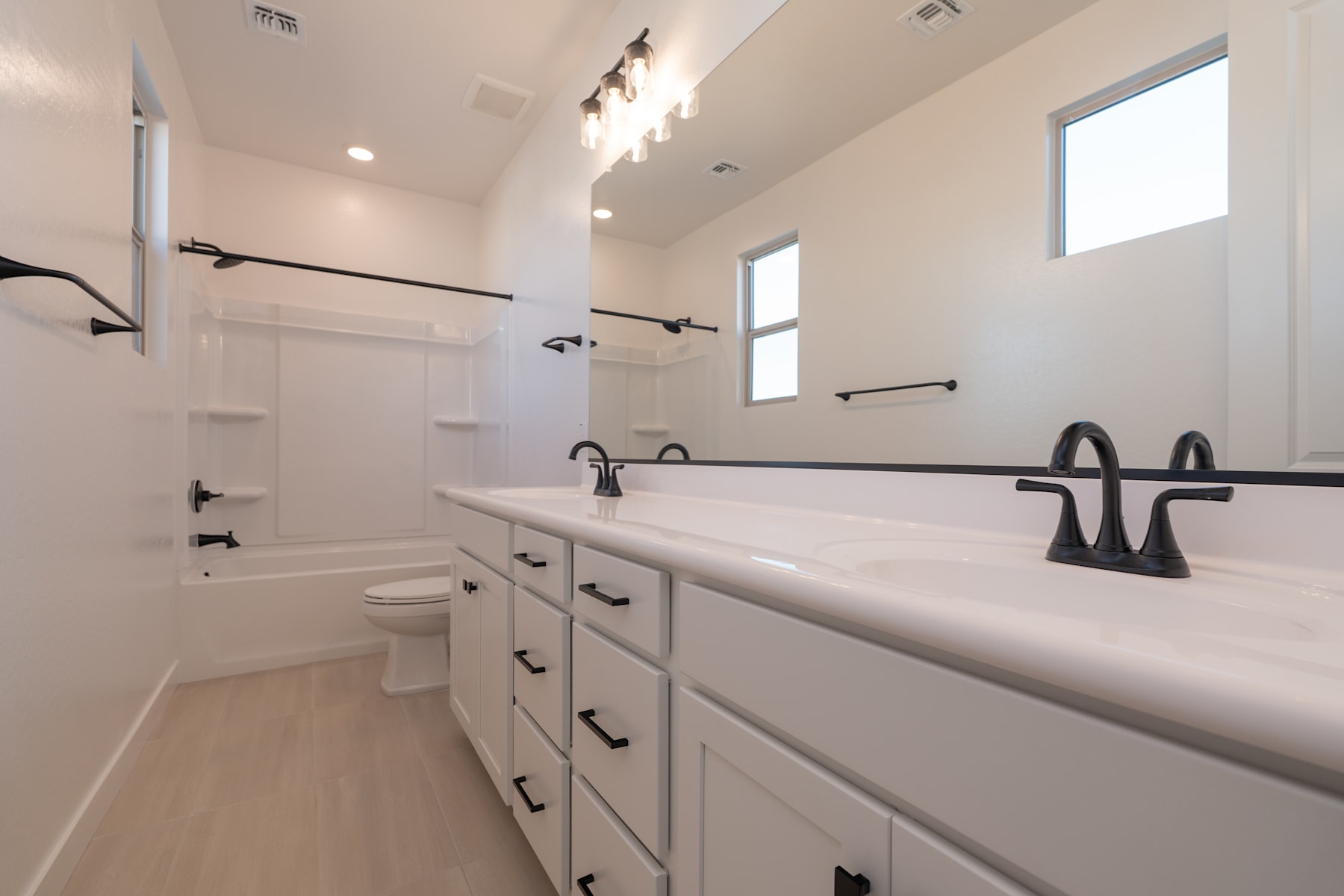 A modern, well-lit bathroom with white cabinets, a double vanity, and black fixtures, set against a bright and airy backdrop.