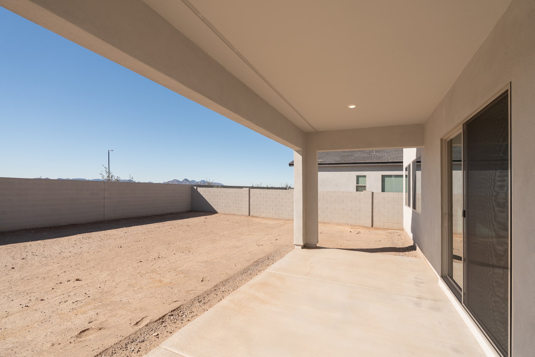 A spacious outdoor walkway with a concrete floor and a clear blue sky in the background, leading to a building with a glass door.