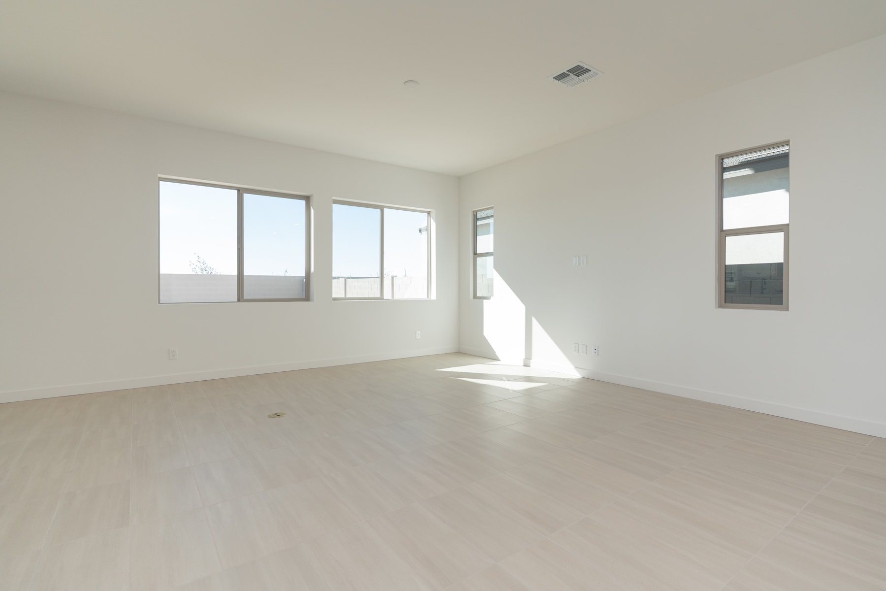 A spacious, well-lit room with large windows, a bare wooden floor, and a clean, minimalist aesthetic.