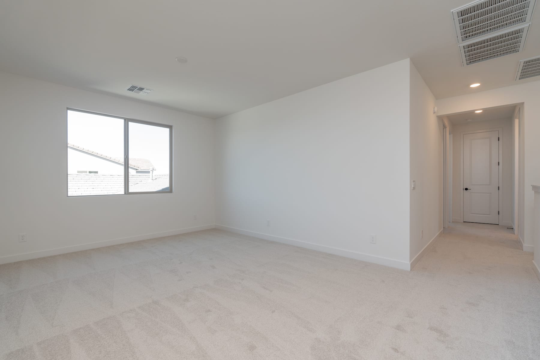 A spacious, minimalist room with white walls, a large window, and a hardwood floor.